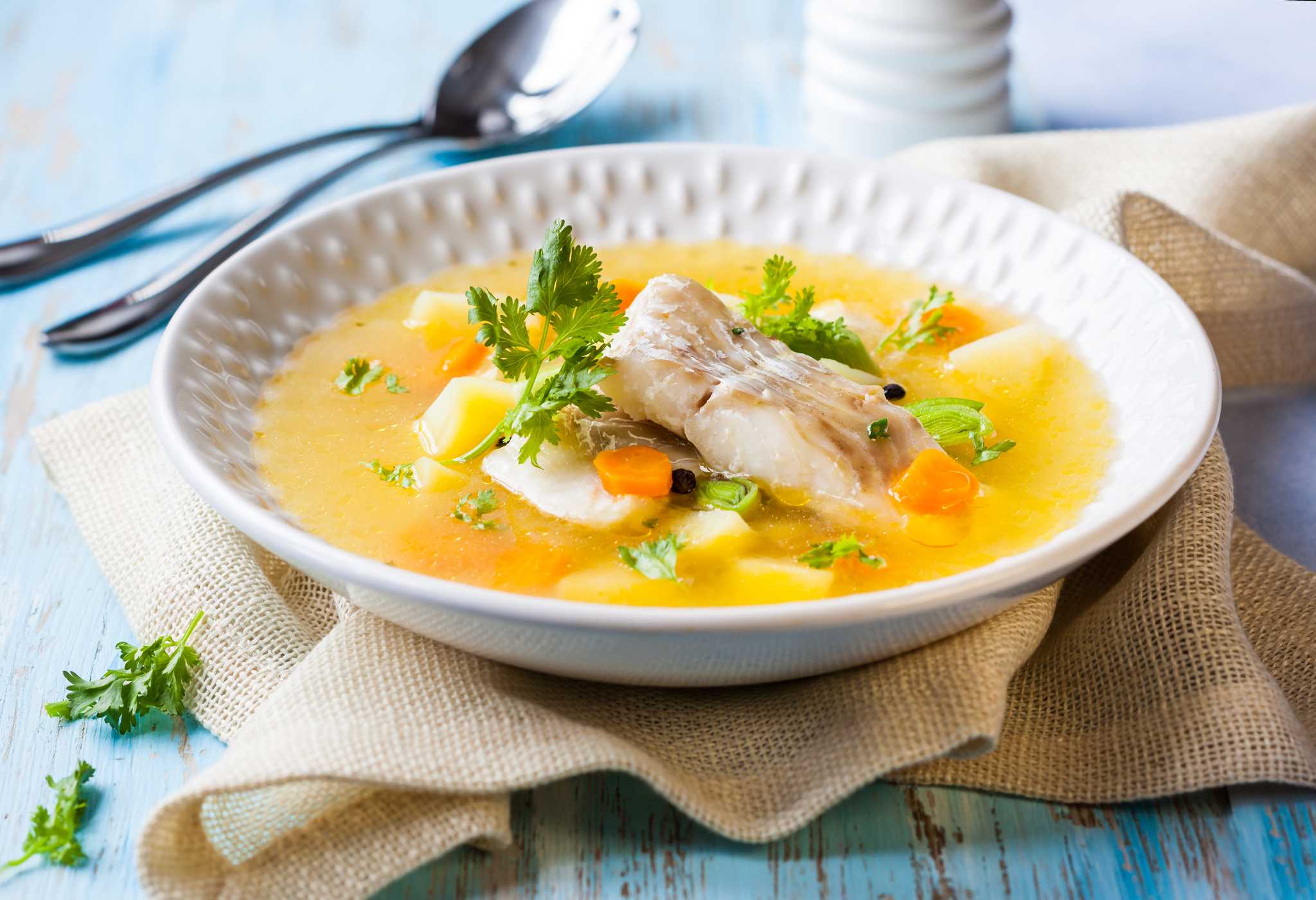 Fish soup with potatoes, carrots, and fresh herbs in a bowl.