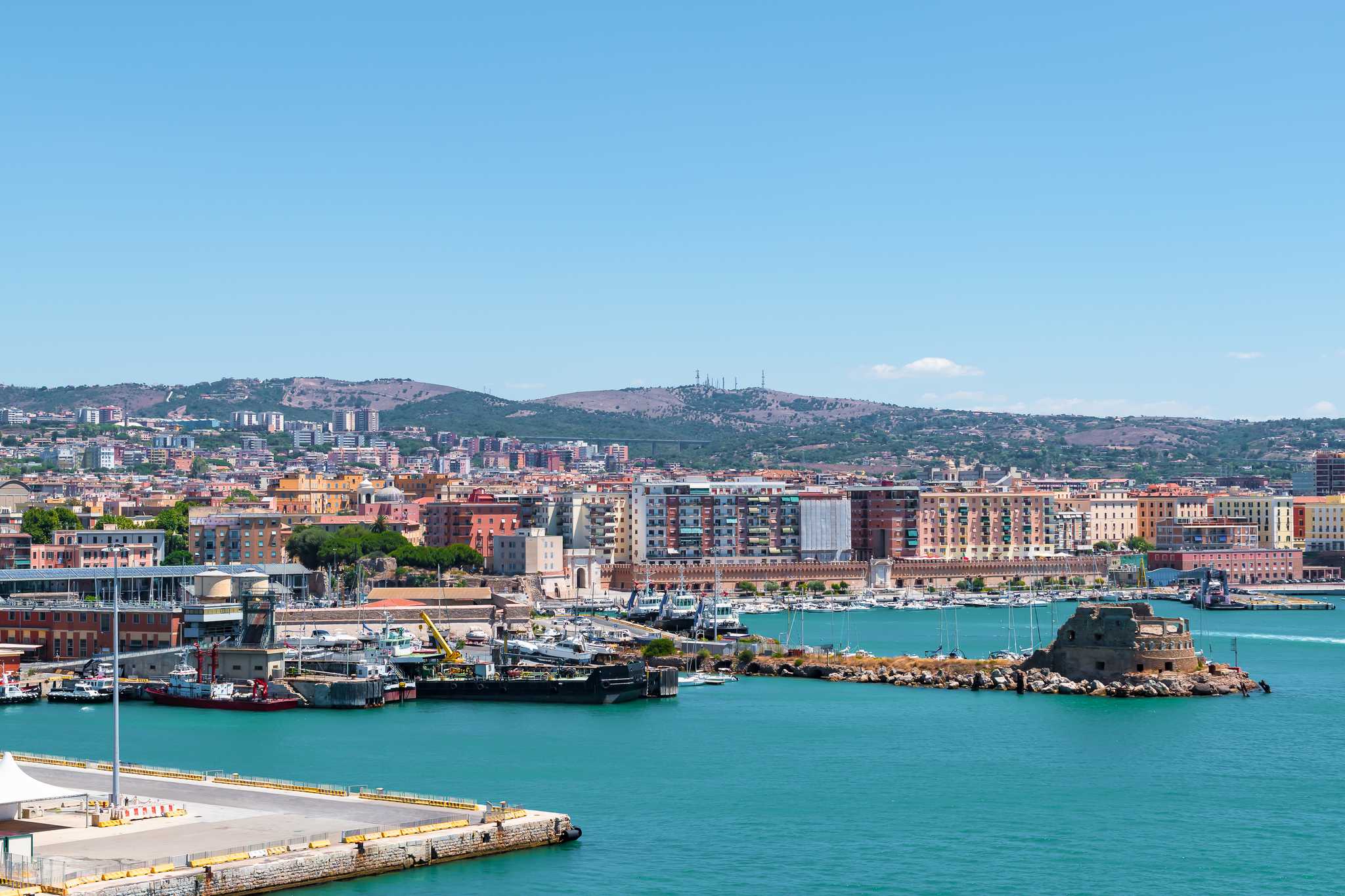 Civitavecchia's coast with waterfront apartment buildings and a marina beneath a clear blue sky.