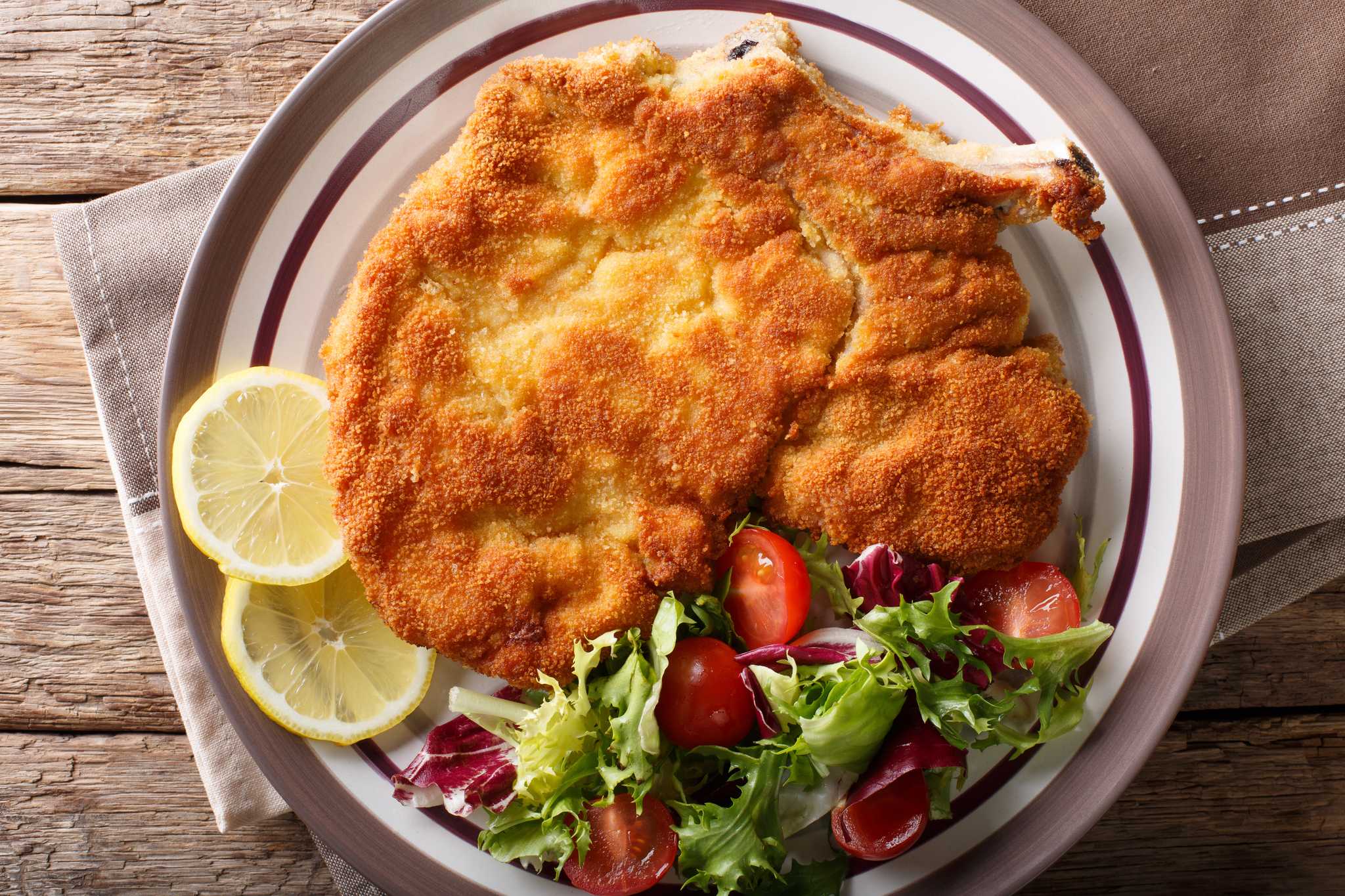 A golden-brown breaded veal cutlet served with salad and a slice of lemon.