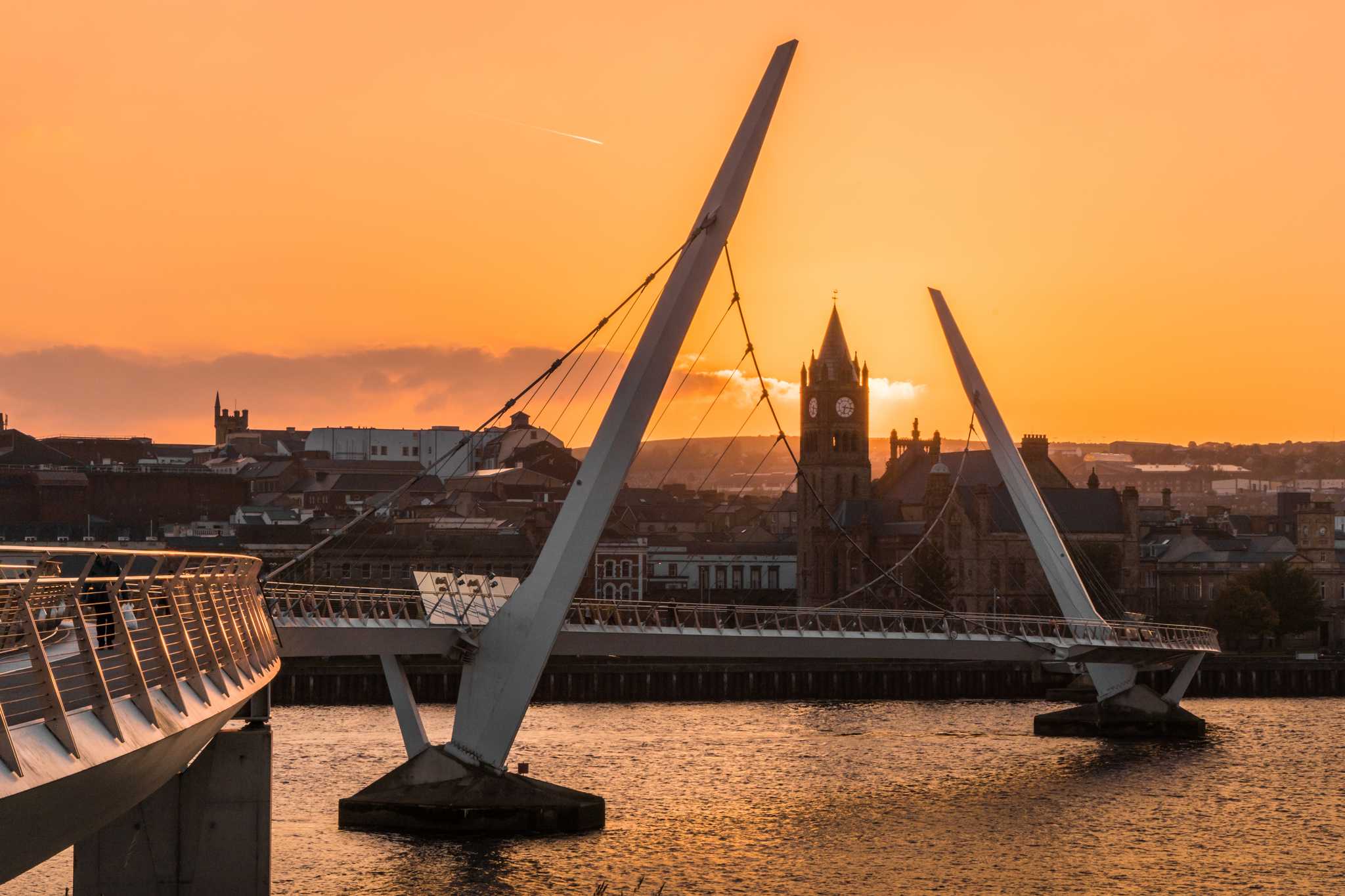 Derry’s bridge framing its clock tower at sunset, bathed in orange light.