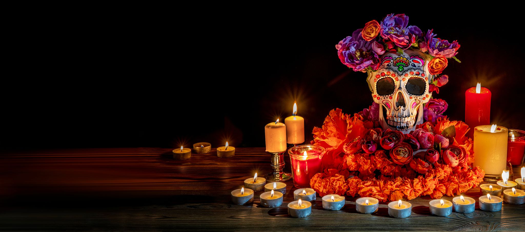 Painted skull with a flower crown, marigolds, and candles for Día de los Muertos.