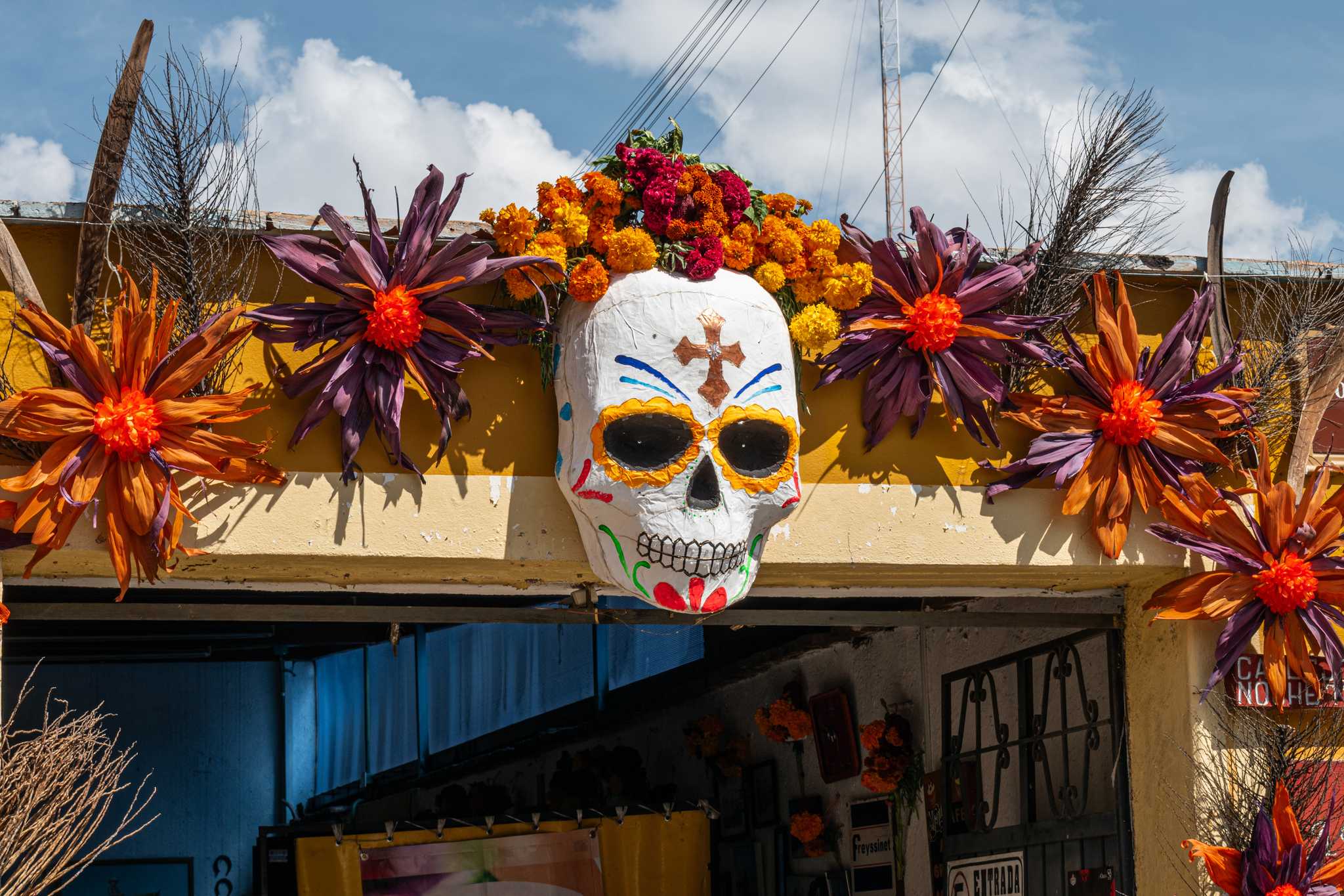 Painted papier-mâché skull and corn husk flowers above a doorway in Oaxaca.