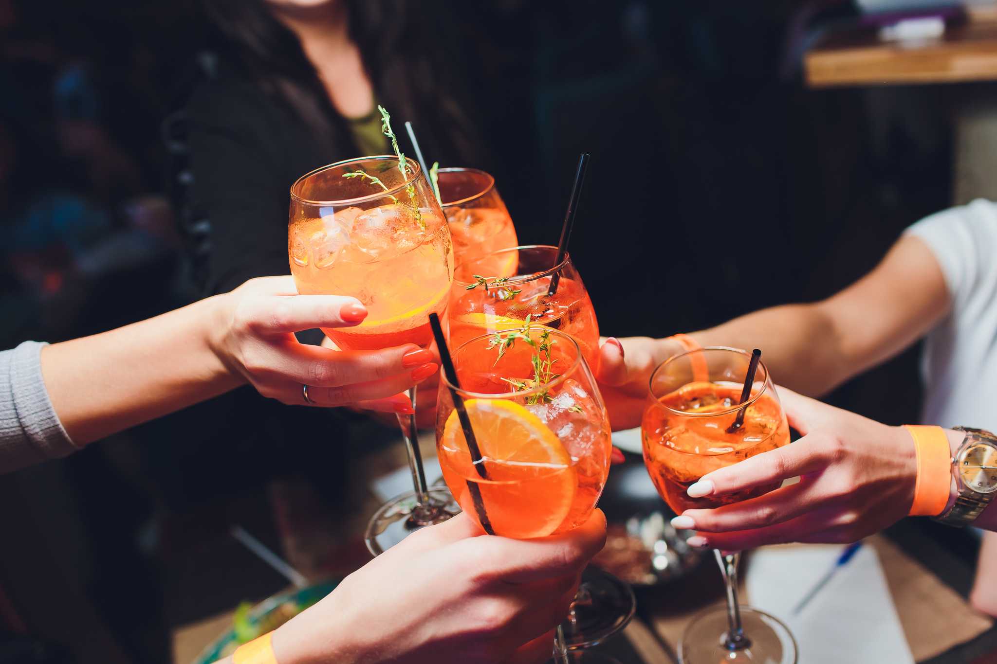 A group of people clinks glasses of Aperol Spritz together in a bar.
