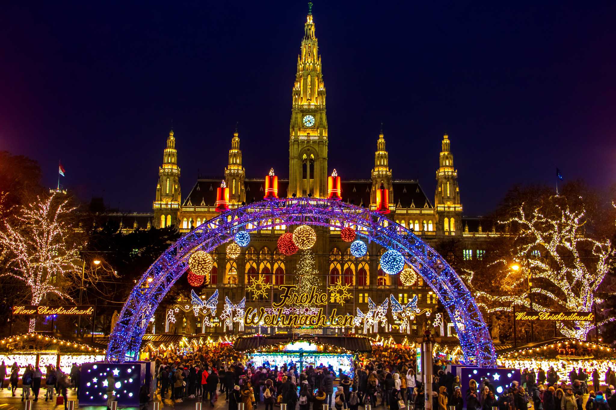 Lighted entrance to Vienna Christmas market at night, with the city hall behind.