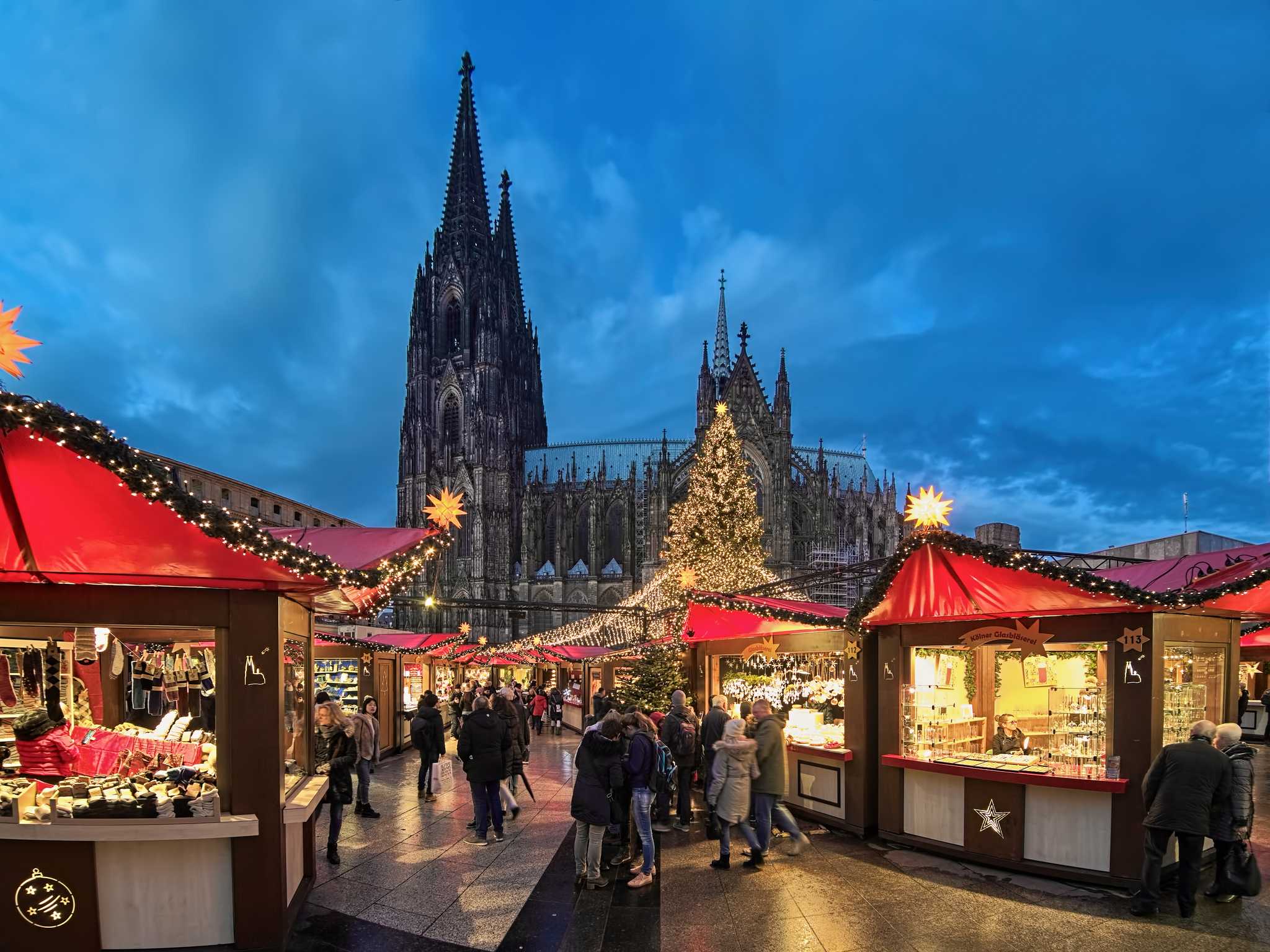 Dusk at the Cologne Christmas market stalls, with the cathedral rising behind lit stalls.
