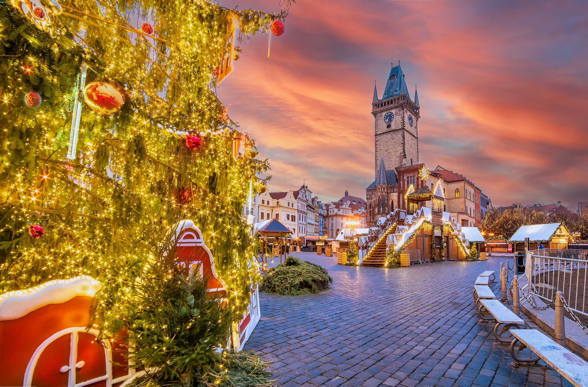 A sunset shot of a Christmas tree to the left of market stalls in front of Prague’s Old Town Hall.