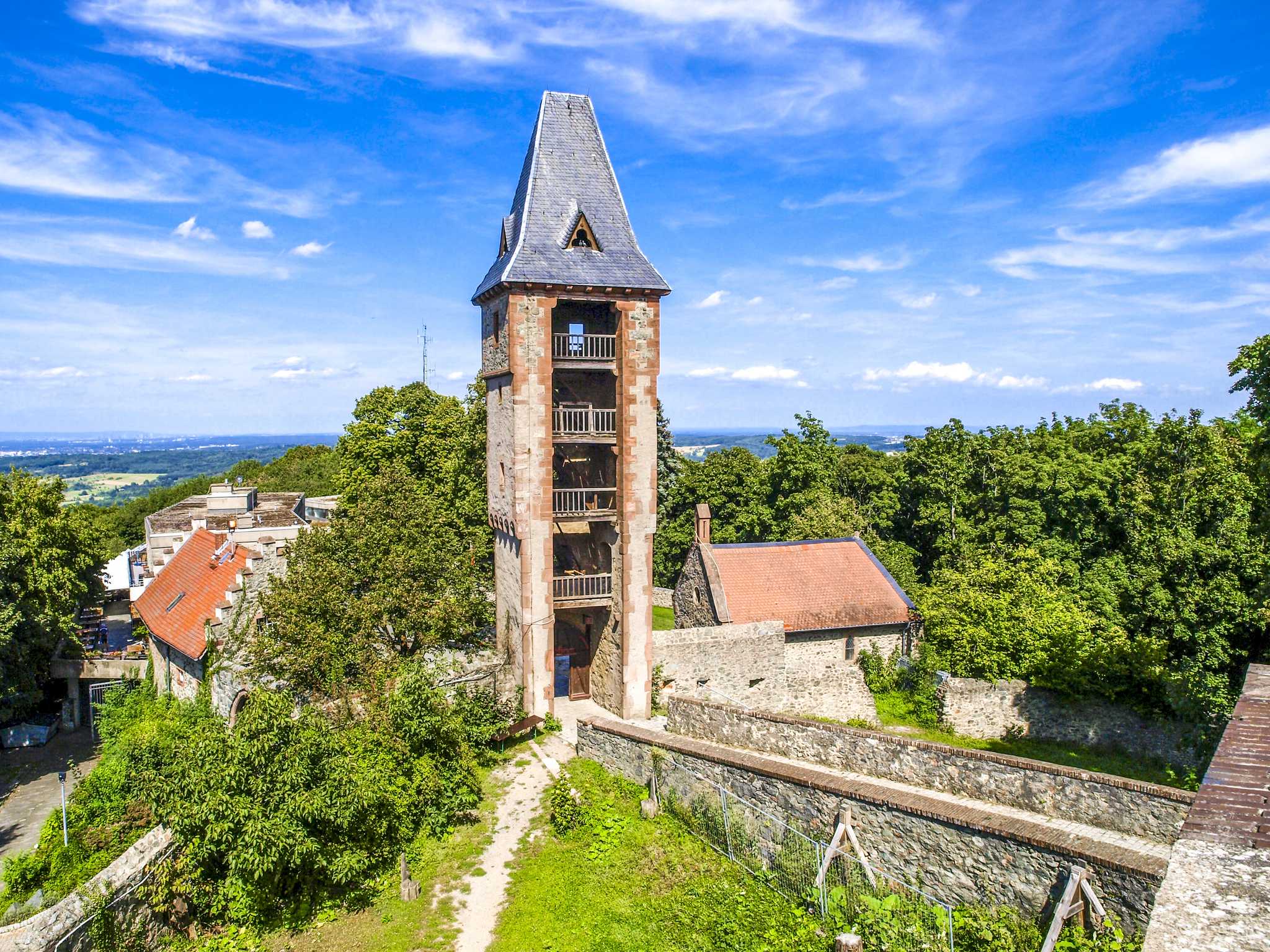 Close-up of Frankenstein Castle tower under a blue sky, with green foliage below.