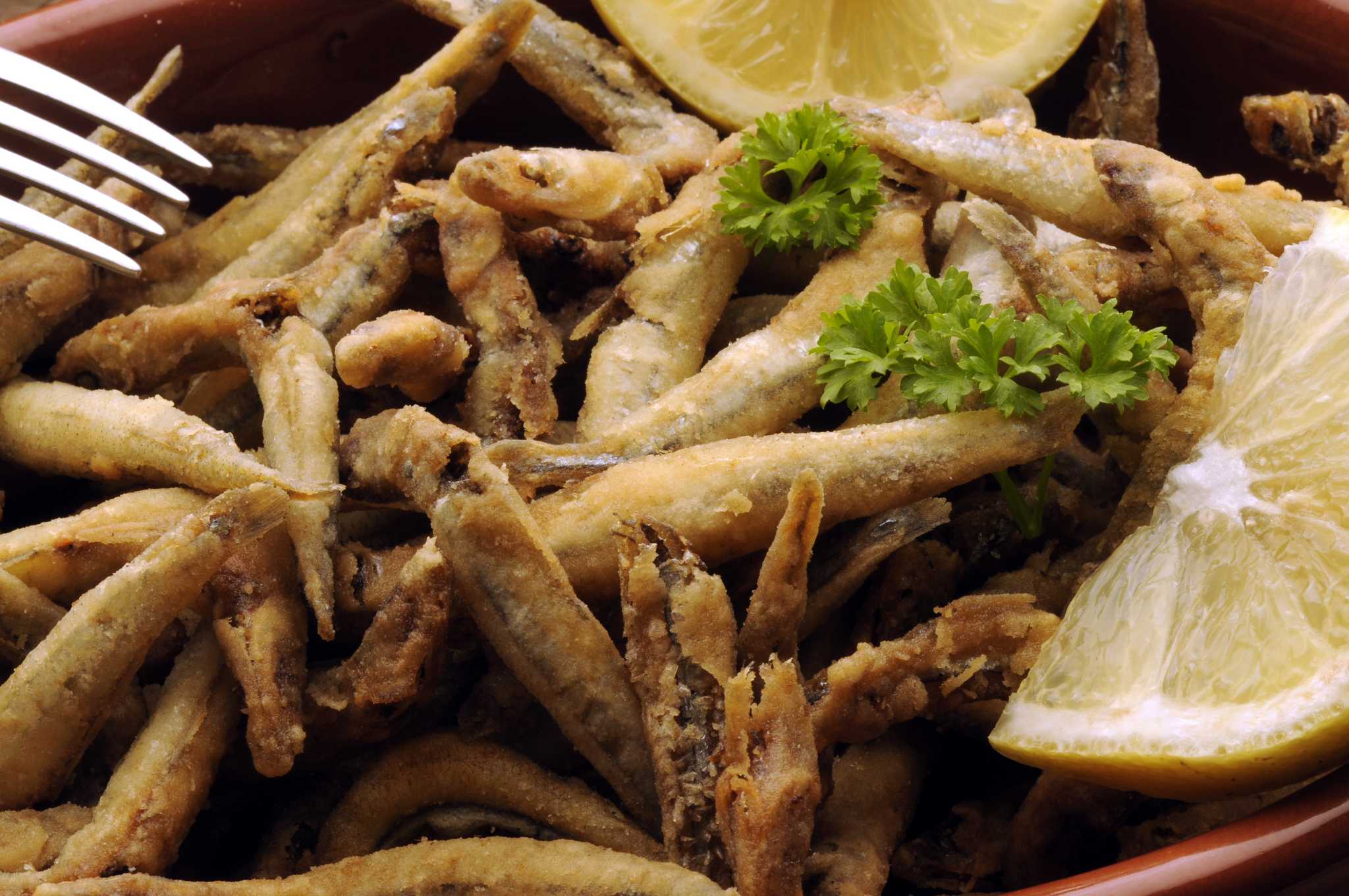 A close-up shot of golden-brown fried whole small fish served with lemon and parsley, an Italian specialty.