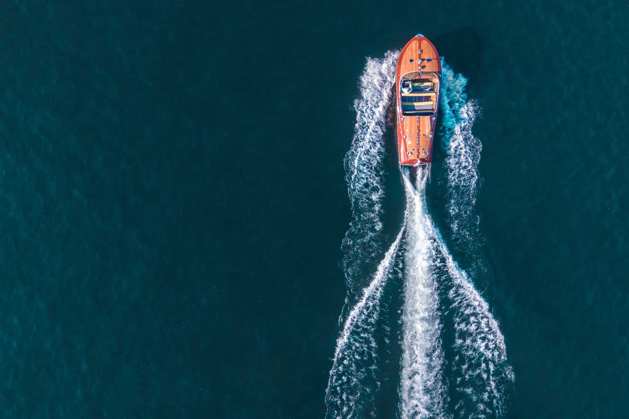 A classic wooden speedboat crossing Lake Como, seen from above with a white wake.