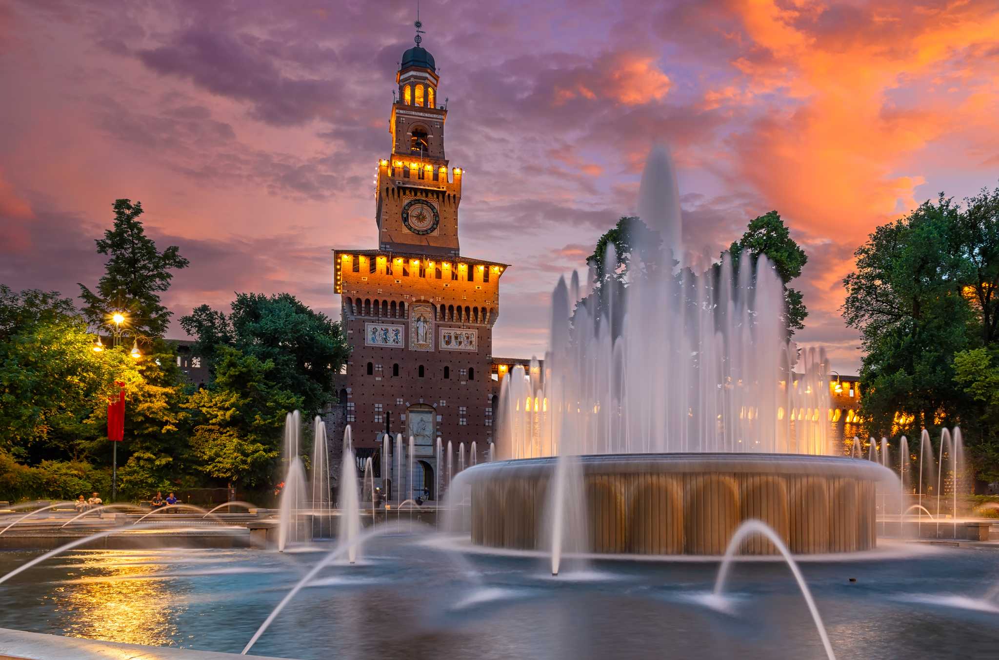 A church with a park and a dramatic fountain in Milan during the evening.