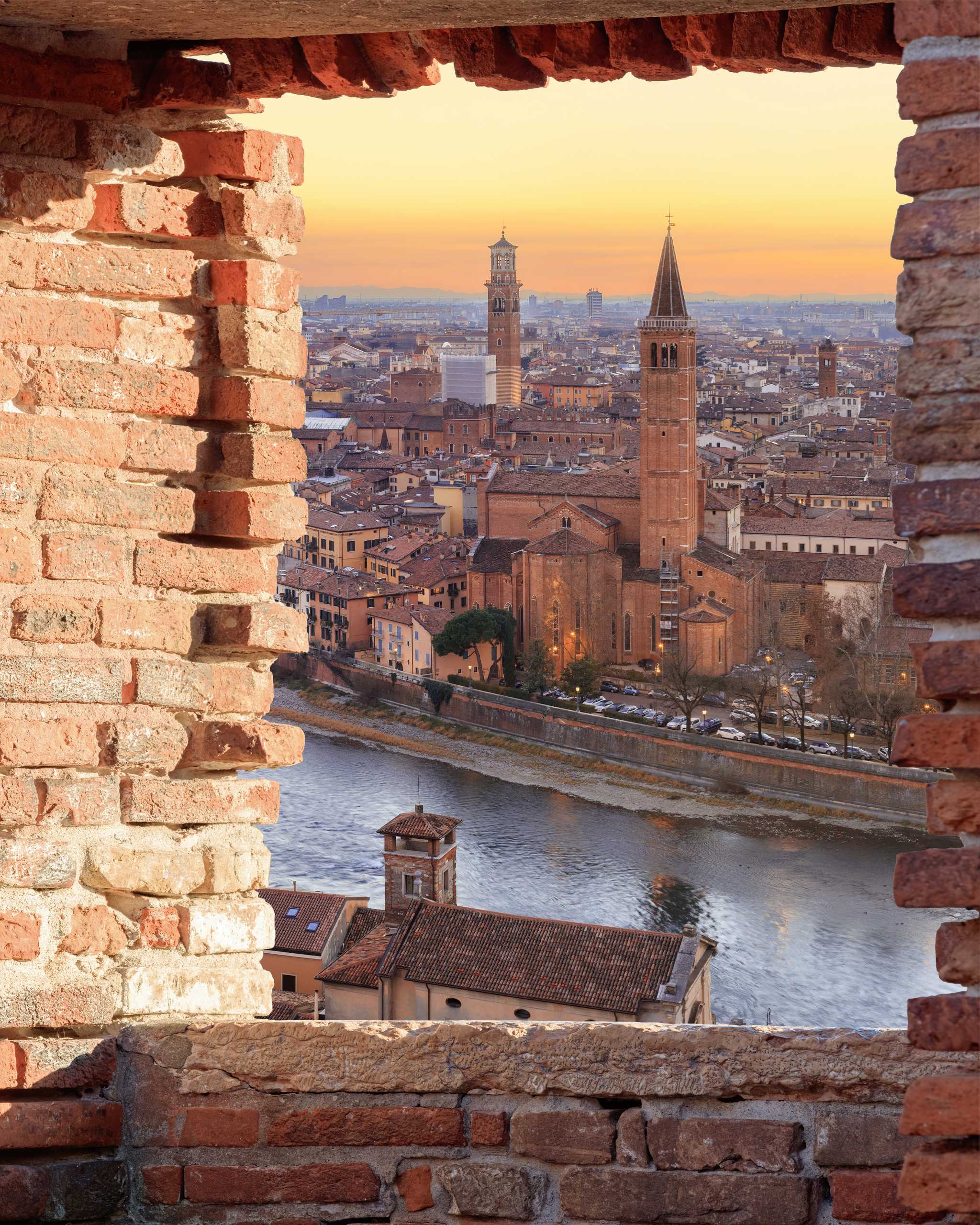 Sunset view of Verona’s historic quarter at sunset, framed by a brick window.