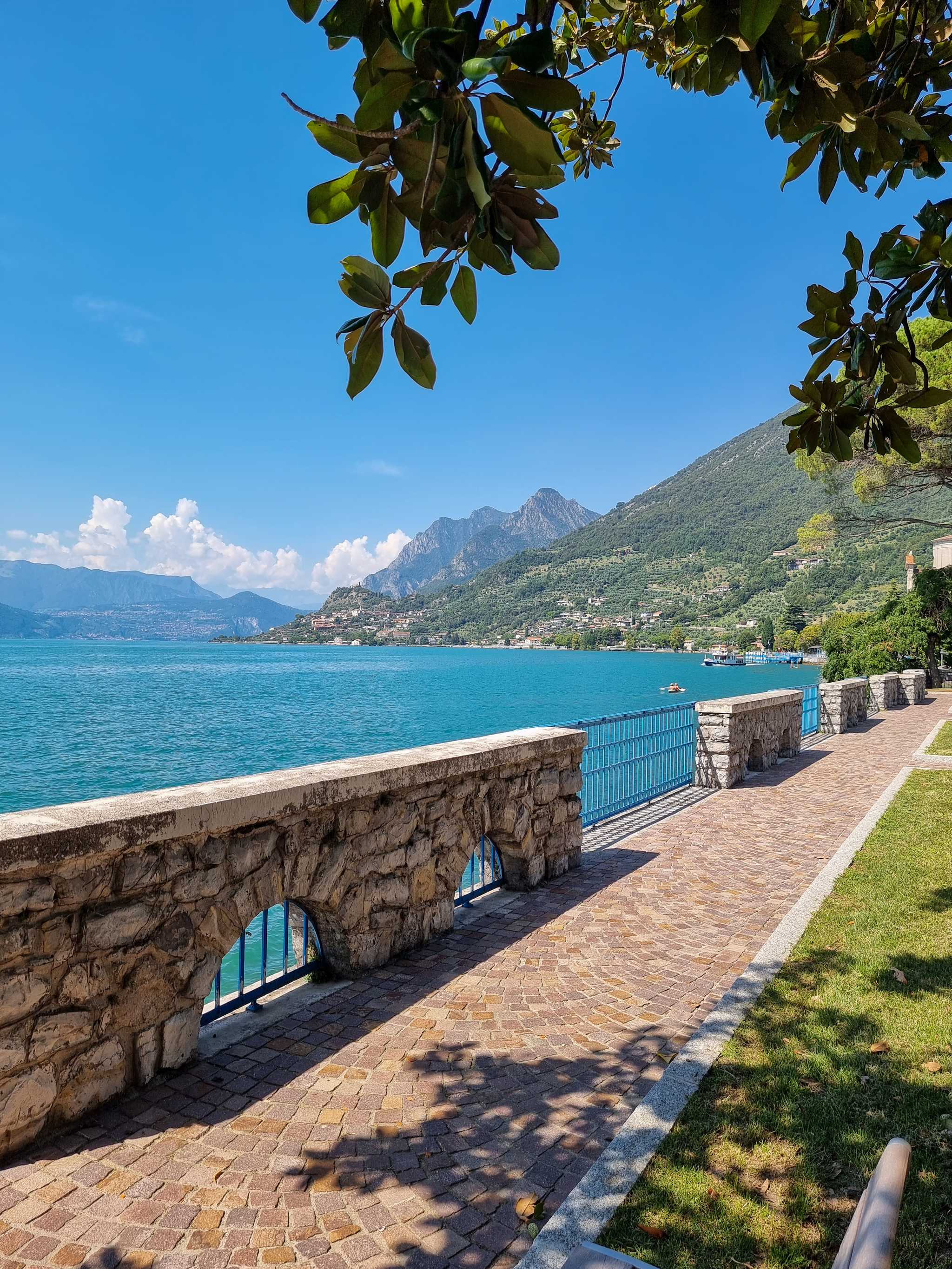 Shore promenade view of bright blue Lake Iseo backed by lush green hills.
