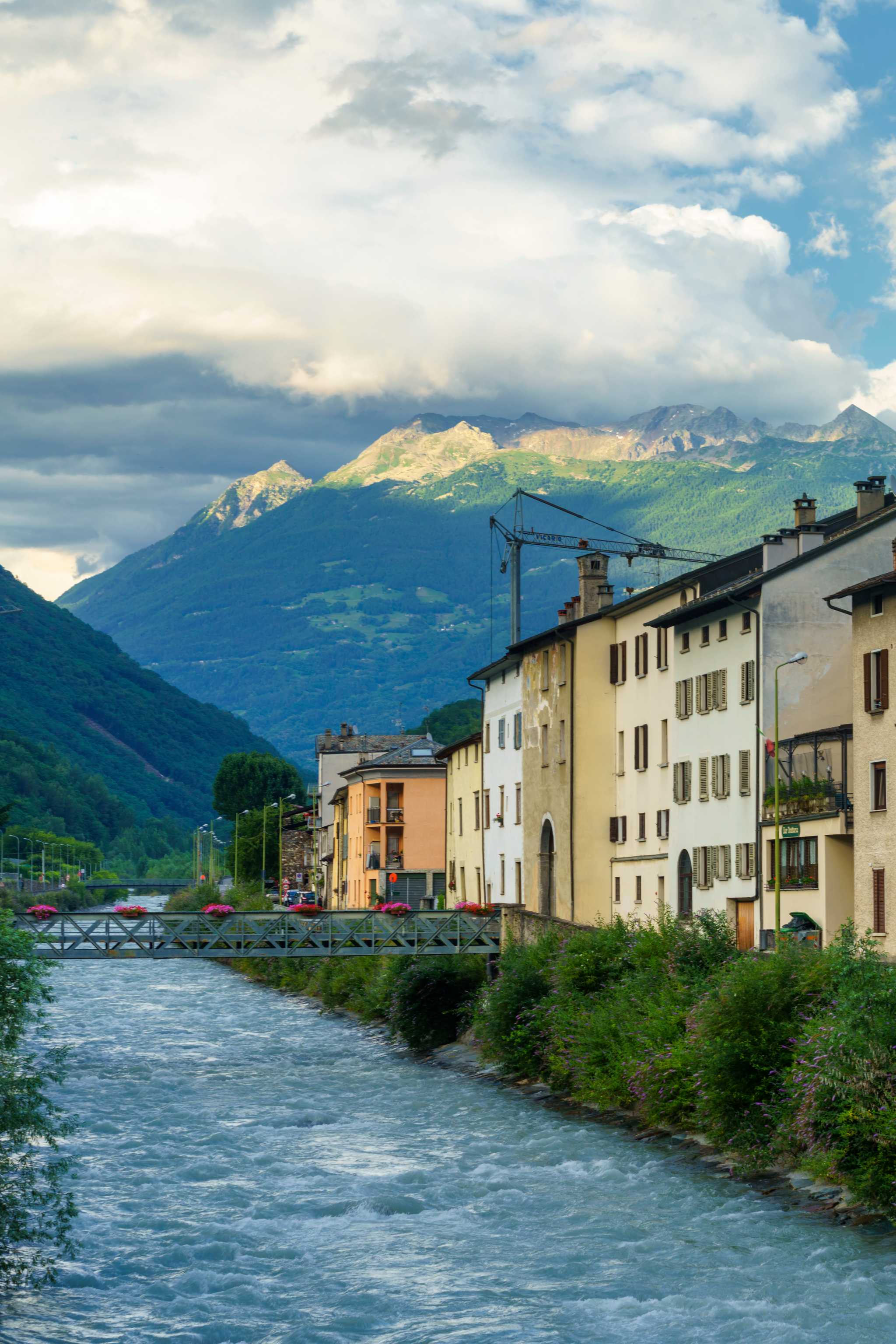 Tirano houses to the right of the Adda river, sunlit green mountains in the background.