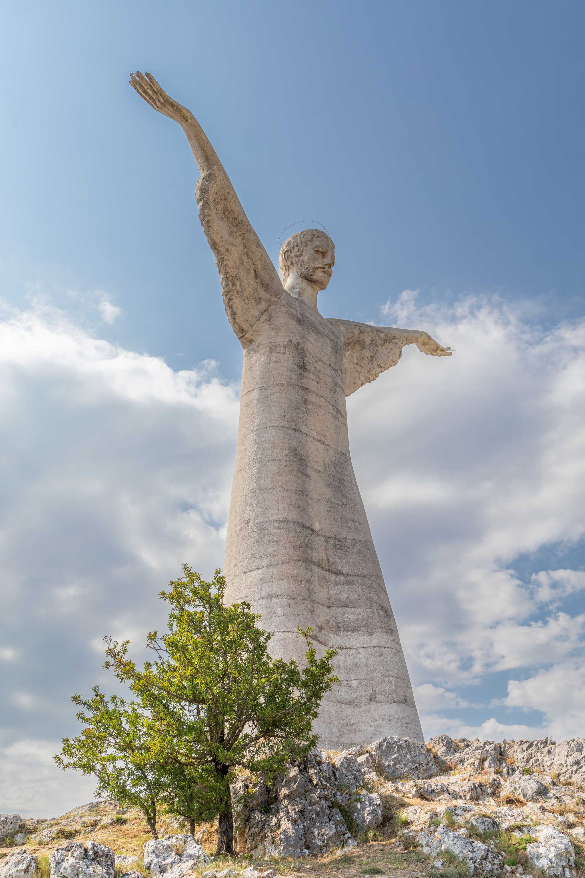 The large white Christ the Redeemer statue of Maratea under a cloudy blue sky.