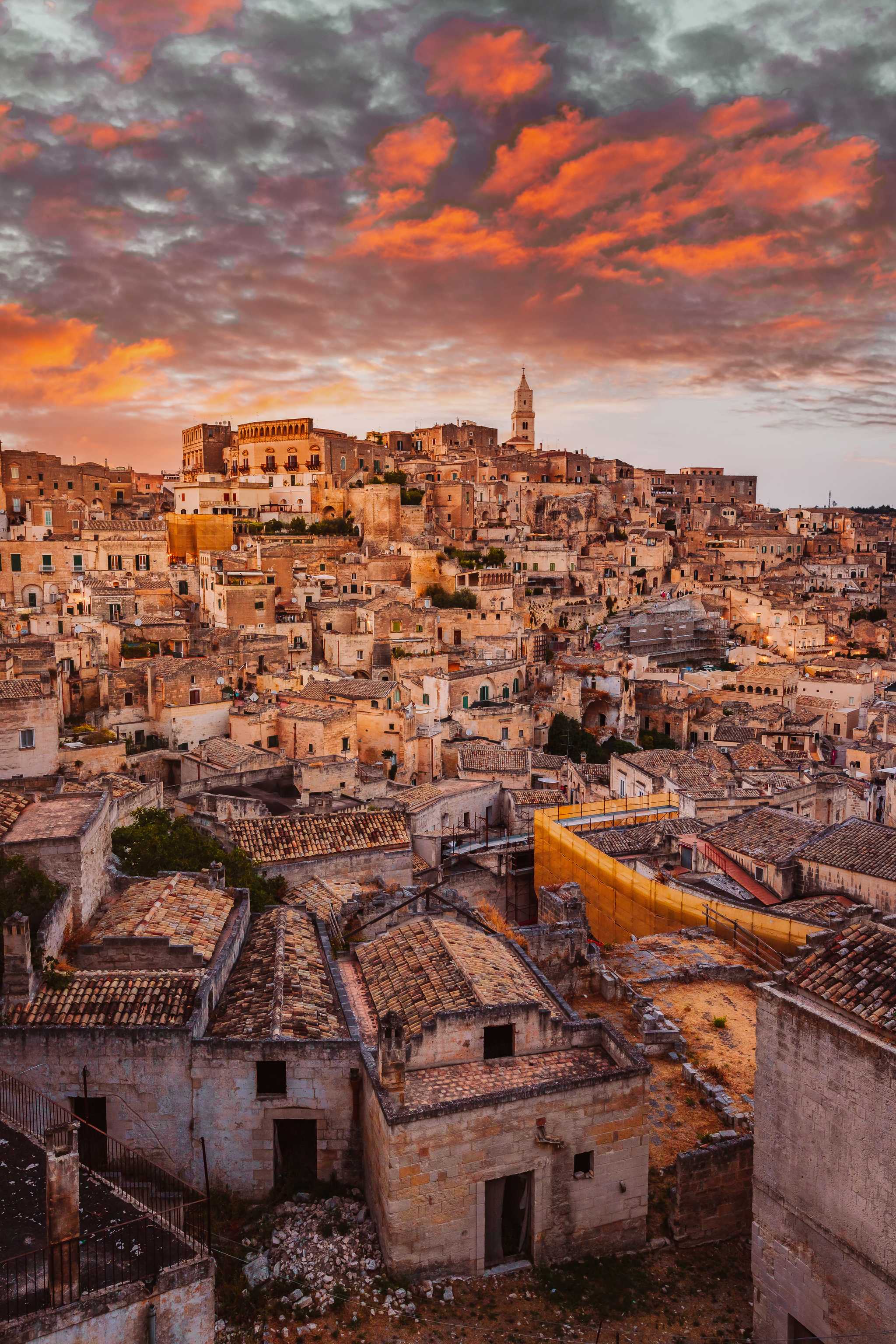 Sprawling Matera cave buildings stacked along a hill under a pink and orange sunset sky.