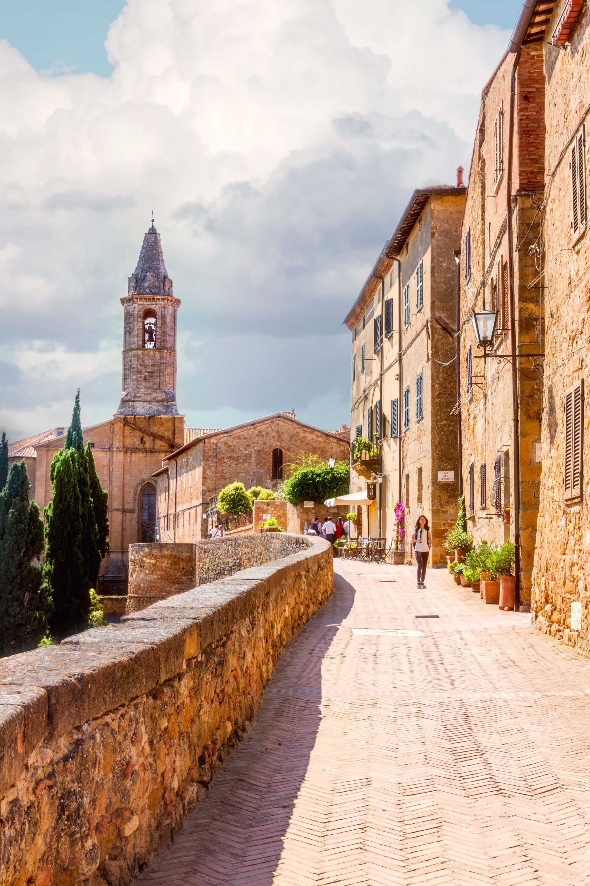 Stone walkway and belltower in Pienza, with white fluffy clouds above.
