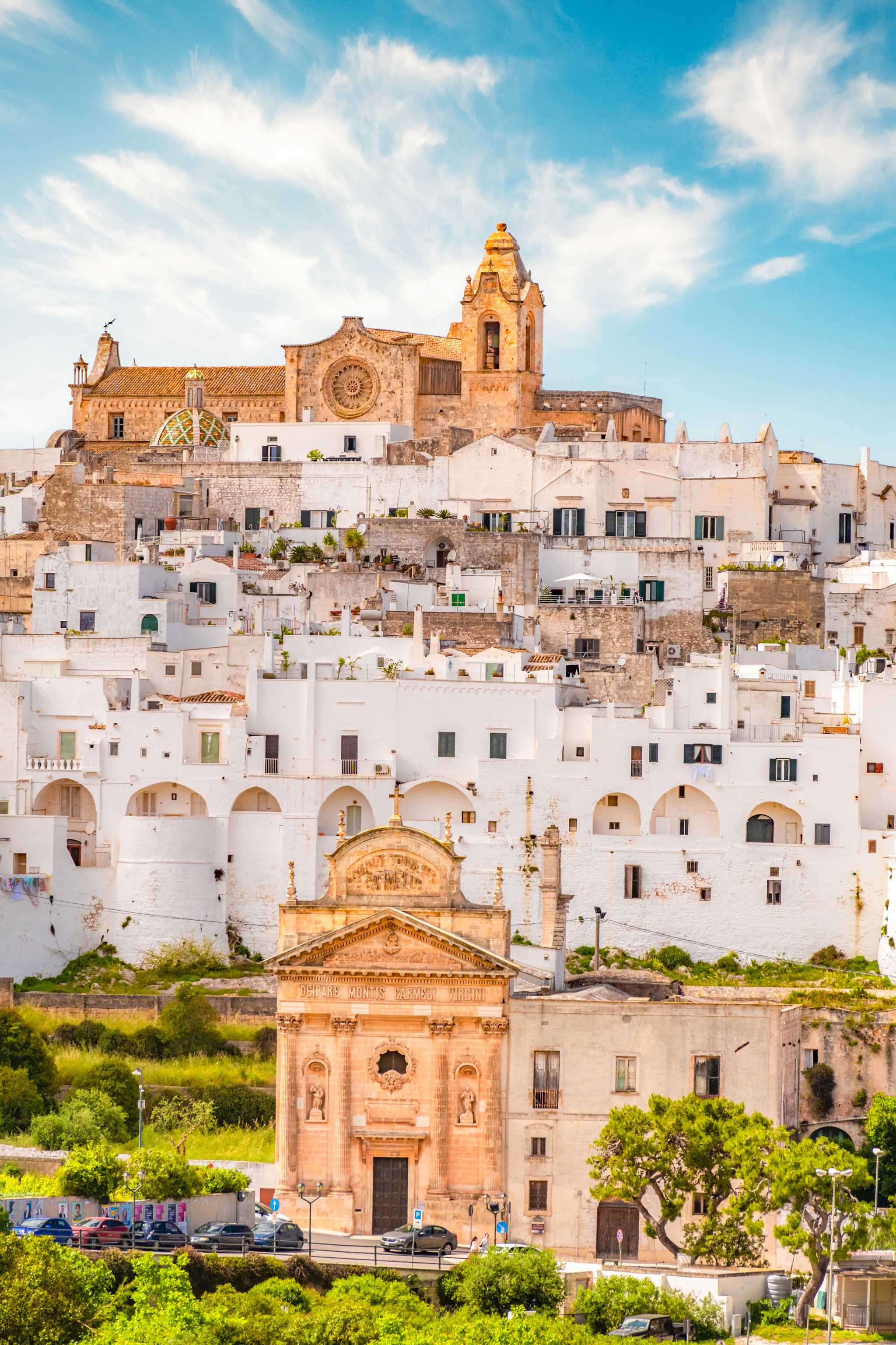 The whitewashed buildings of Ostuni stacked on a hillside under a blue sky.