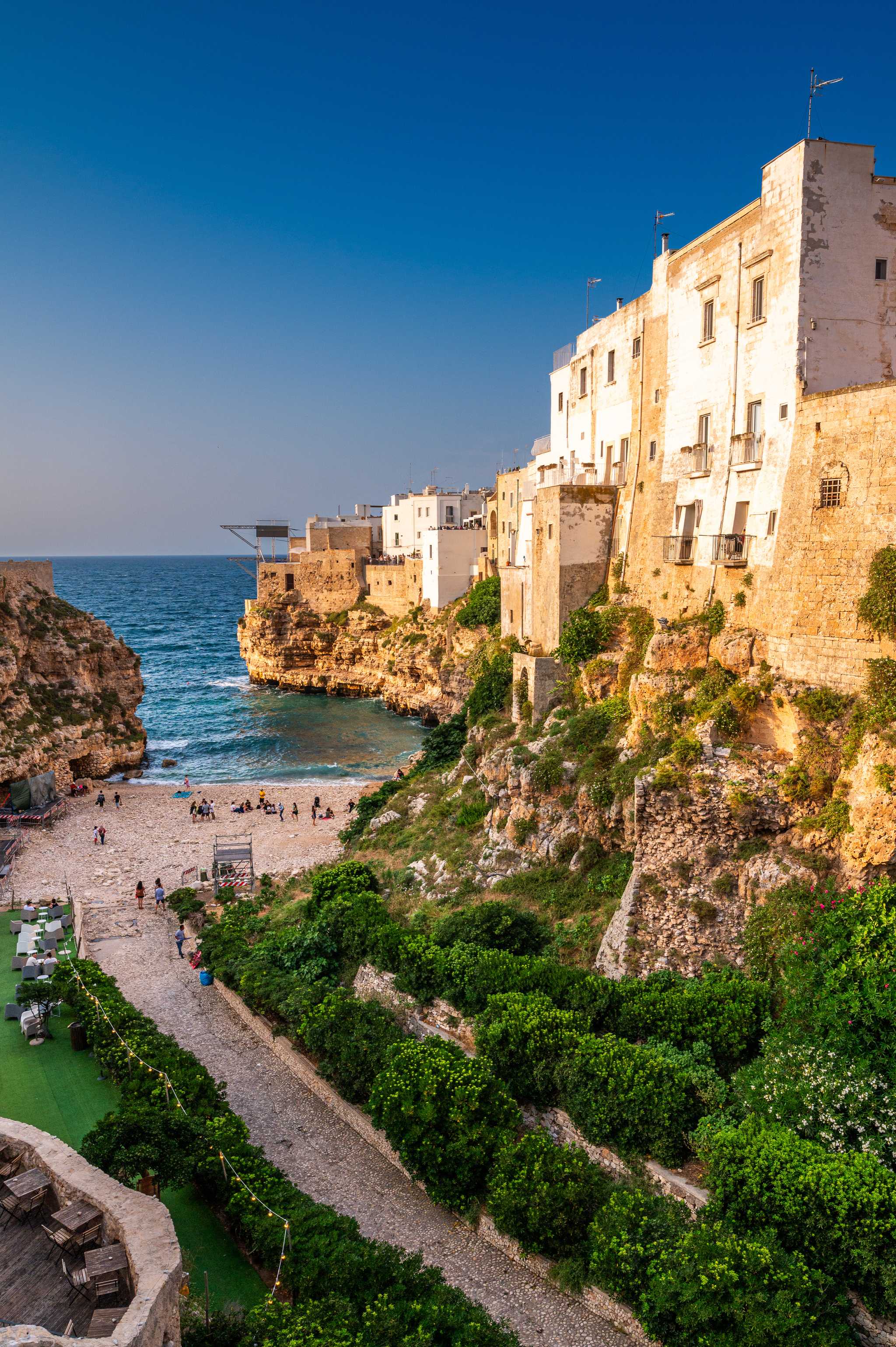 Sandy path down to the Polignano a Mare beach, tucked into a cove, with white buildings on the right.