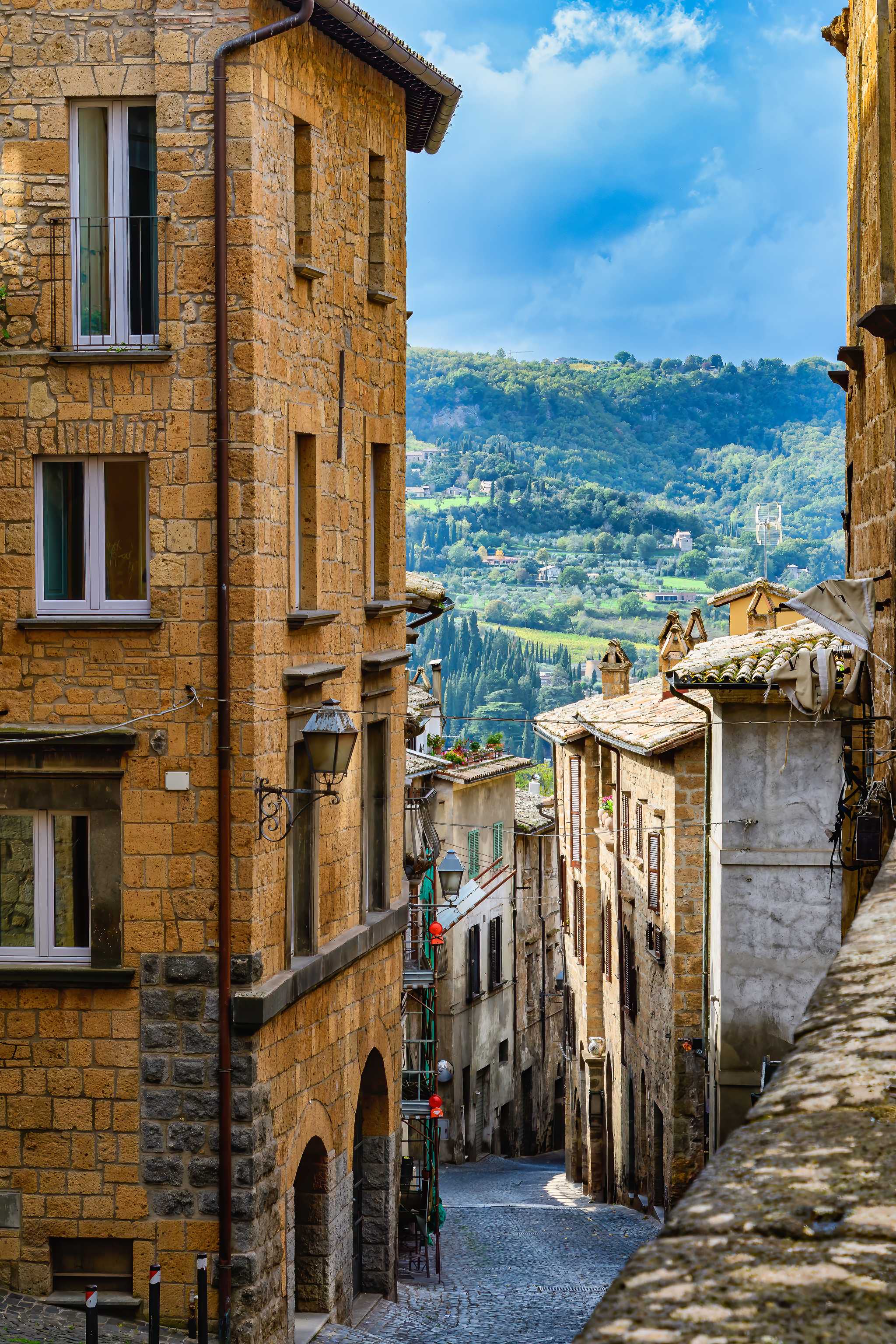 Stone alleyway and stone buildings in Orvieto with distant green hills.