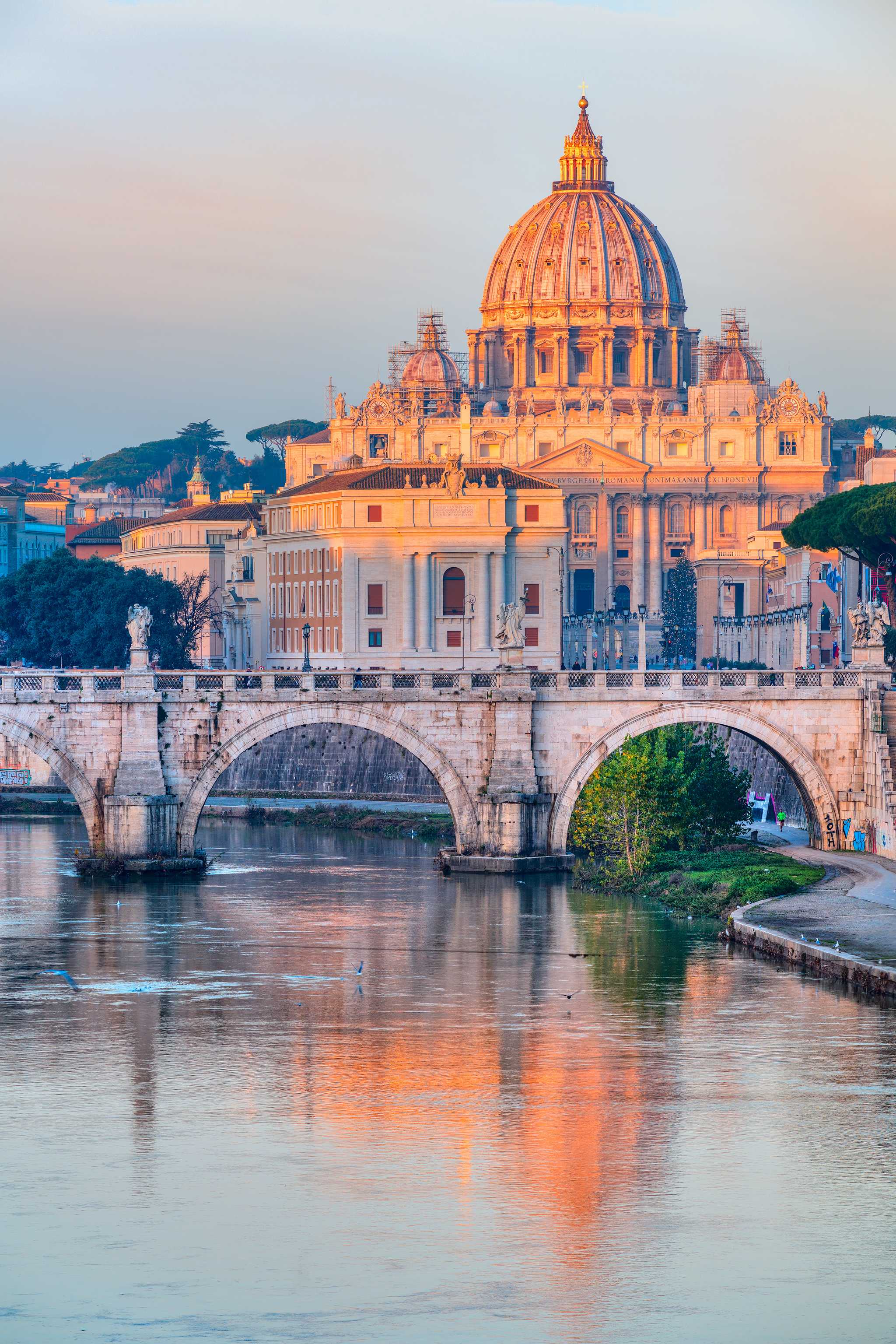 St. Peter’s Basilica lit by a warm sunset, reflected in the river below.