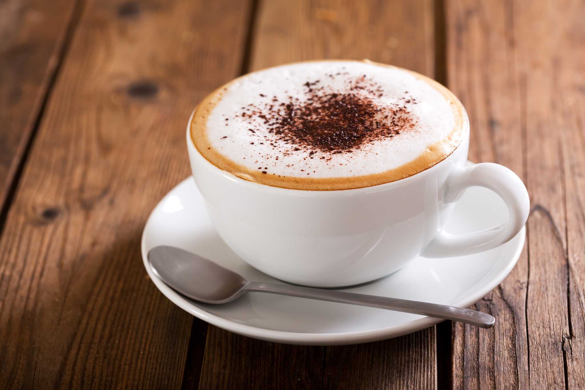 Cappuccino in white mug with chocolate dusting on a wooden table.