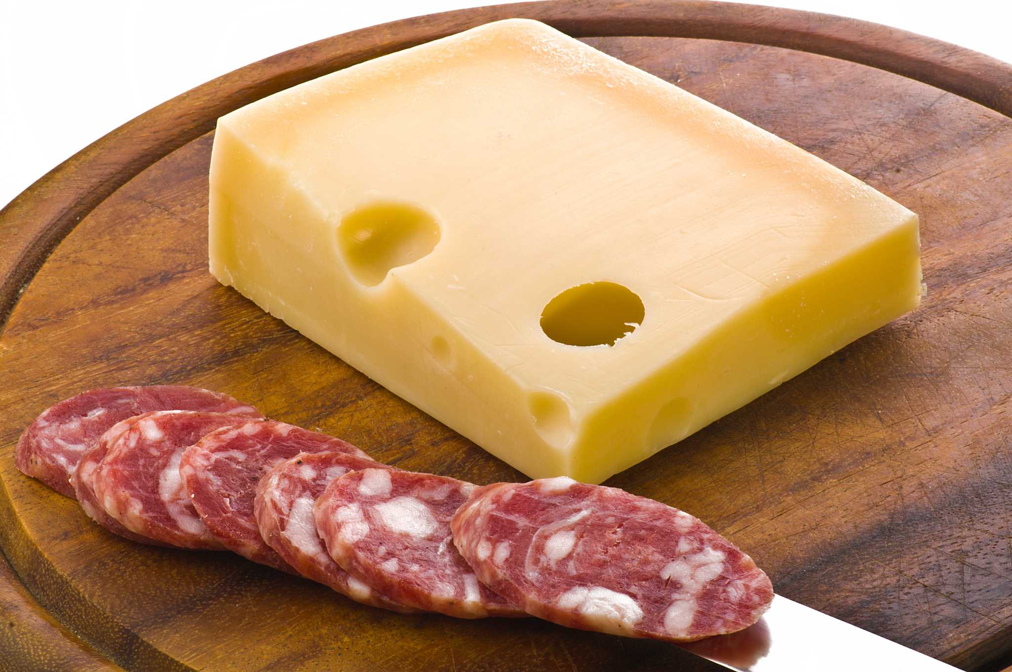 Wedge of cheese and sliced spianata calabrese on a round wooden board.