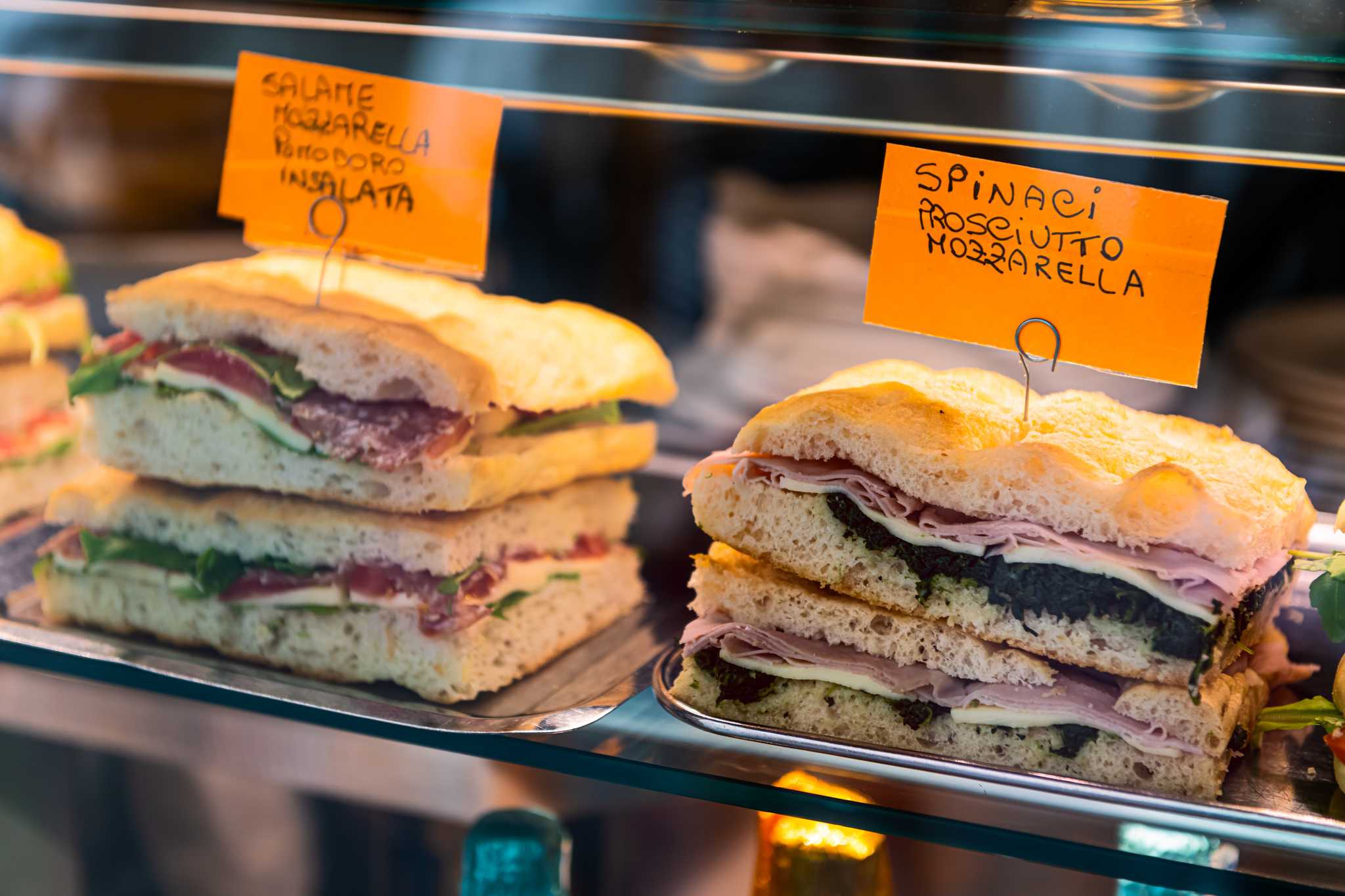 Several ham sandwiches in a glass display case with tags advertising the fillings.