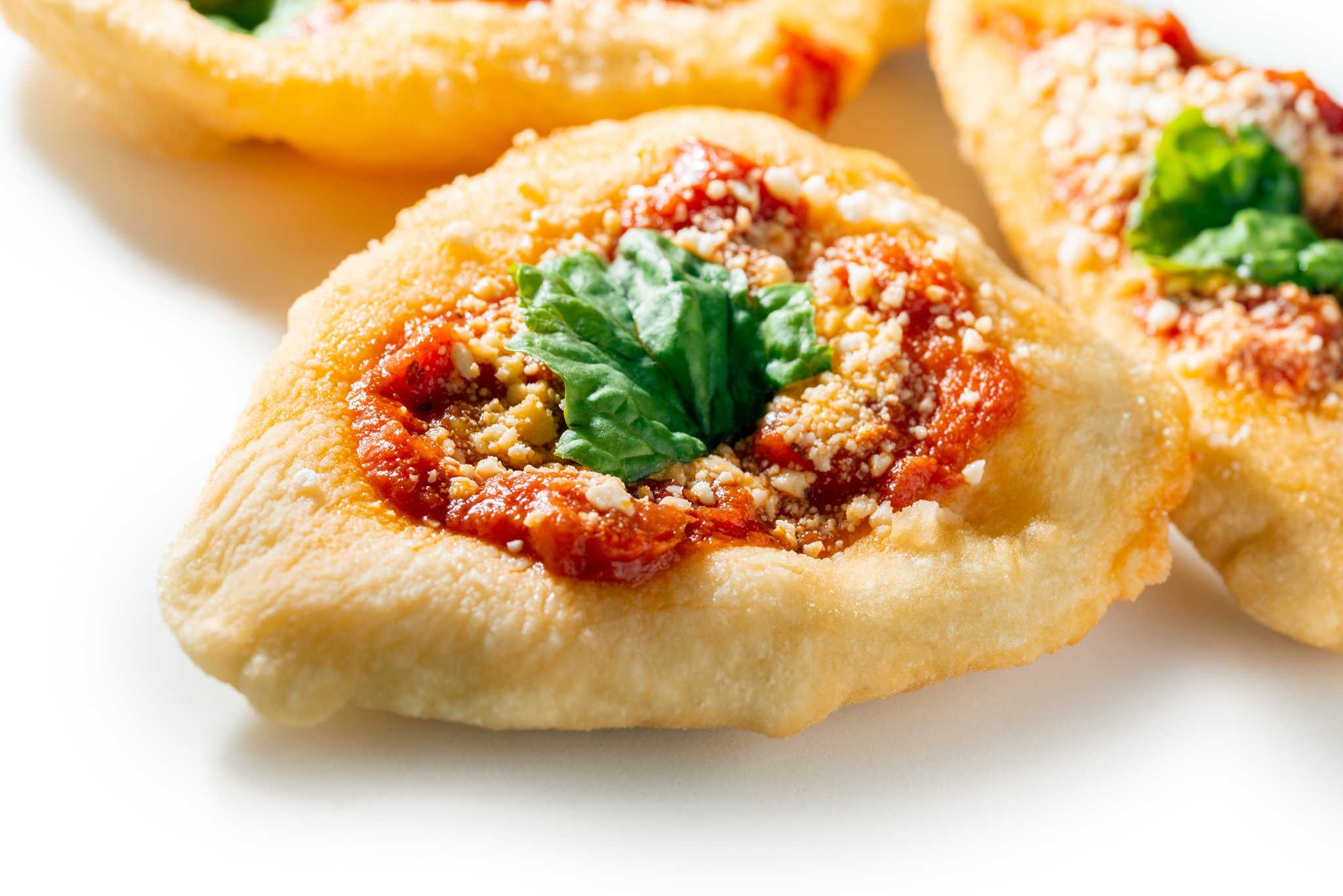 Golden pizza fritta topped with tomato, meat, and basil.