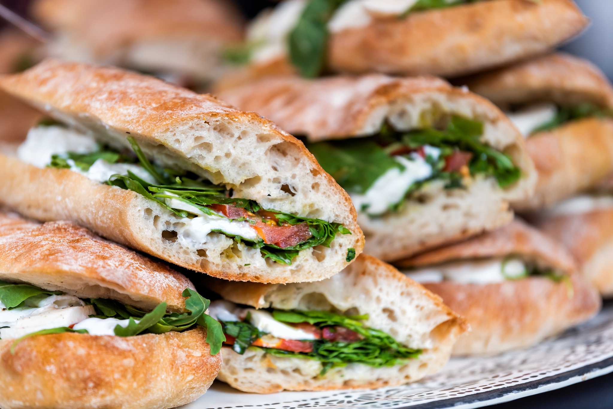 Pile of panini sandwiches with cheese and greens spilling out from the bread.