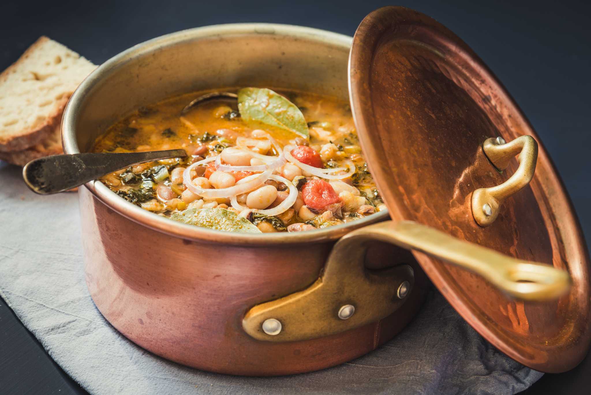 Copper pot full of ribollita vegetable soup with a spoon, bread in the background.