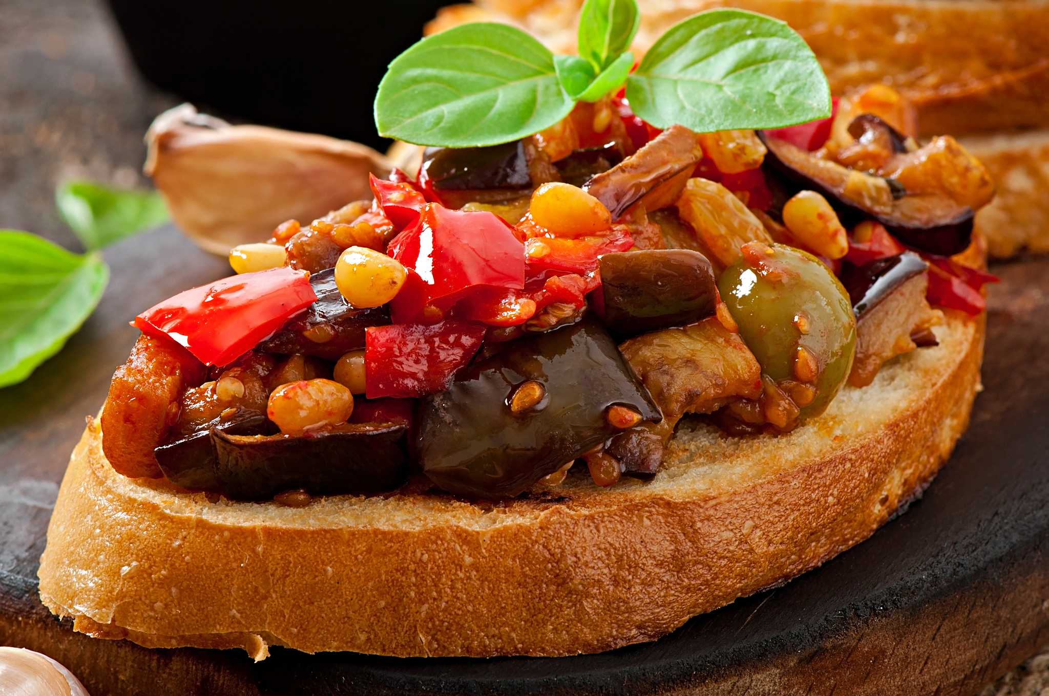 Close-up of caponata on a slice of crusty bread, topped with a basil sprig.