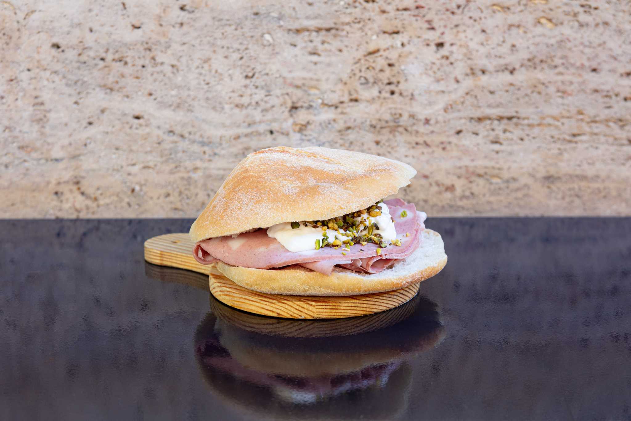 Puccia filled with ham and cheese on a wooden board, sitting on a shiny black surface.