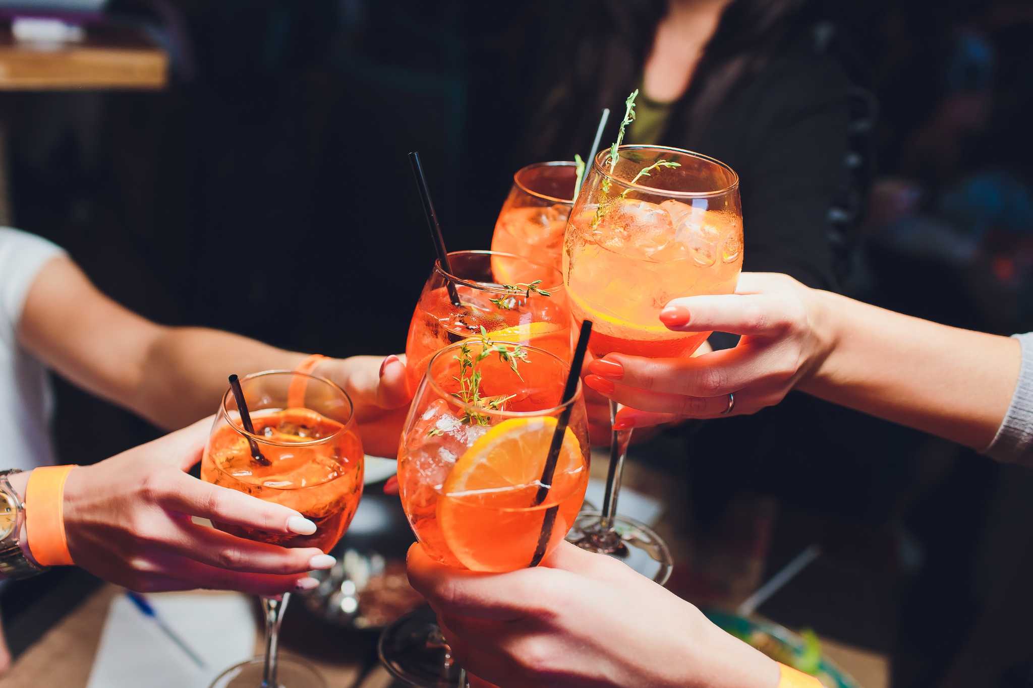Hands holding Aperol spritz glasses, clinking the glasses together in a cheers.