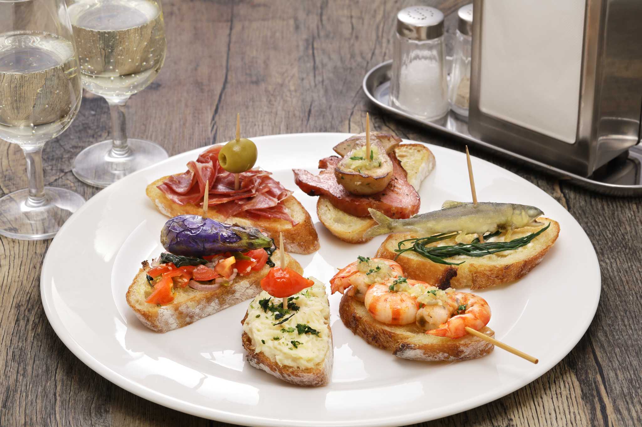 White plate of sliced bread topped with various fish, shrimp, pastes, and meat.
