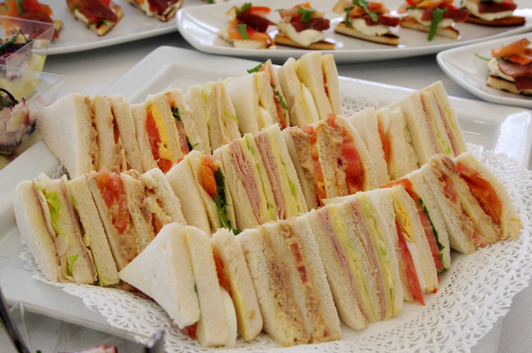 Sideways stacks of triangular sandwiches with various fillings on a cloth-lined platter.