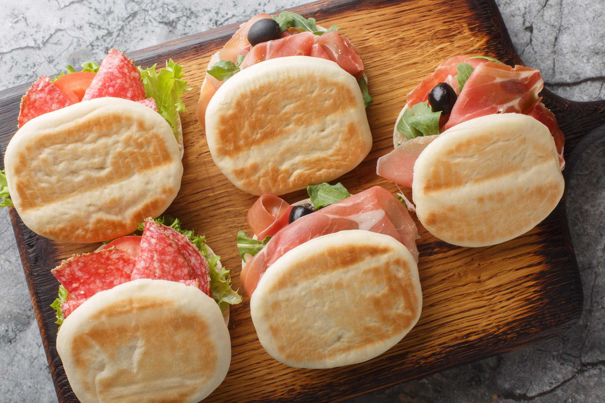 Five tigelle filled with sliced cured meats on a wooden serving board.
