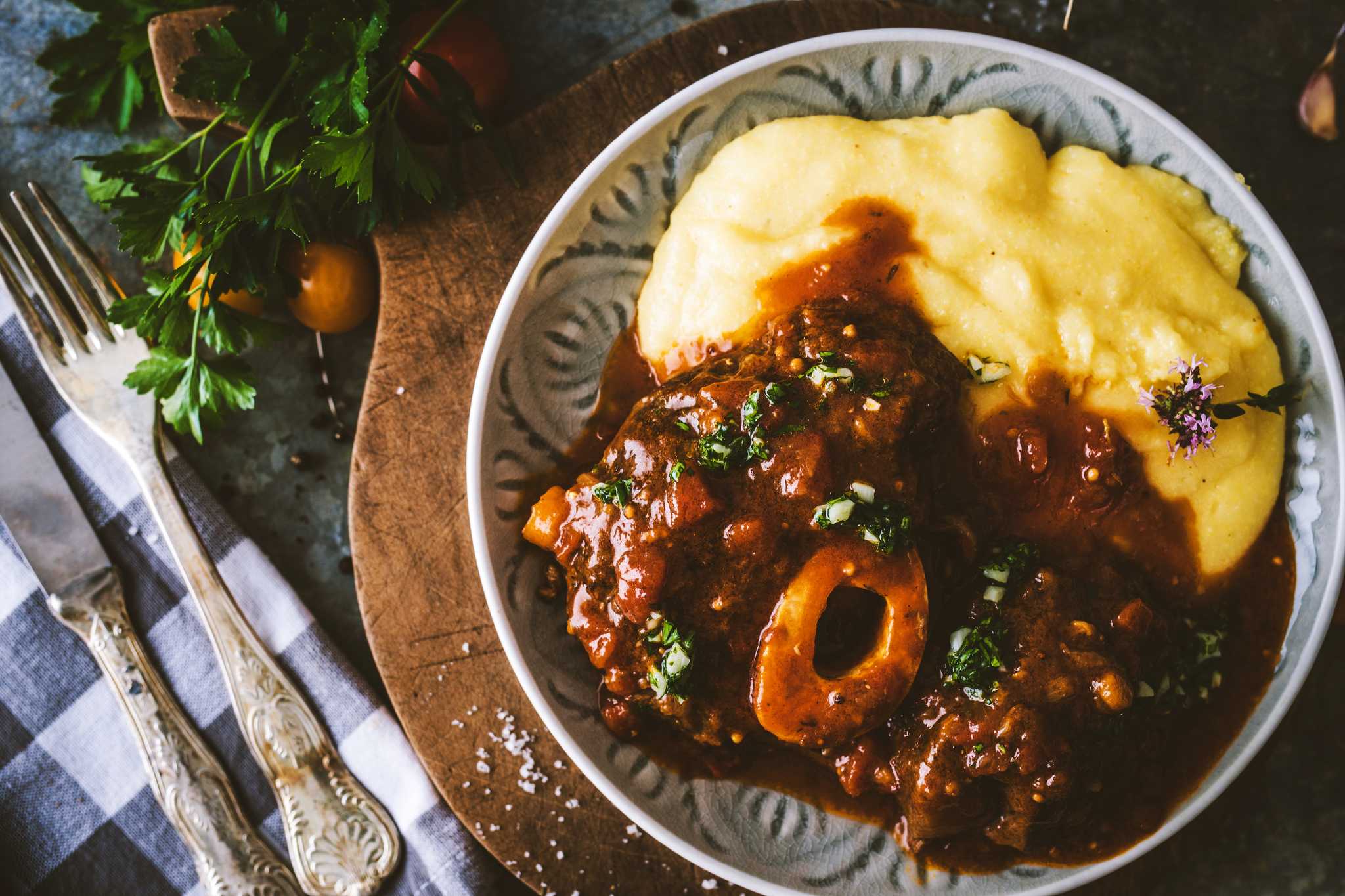 Bowl of saucy osso buco served with creamy polenta beside silverware.