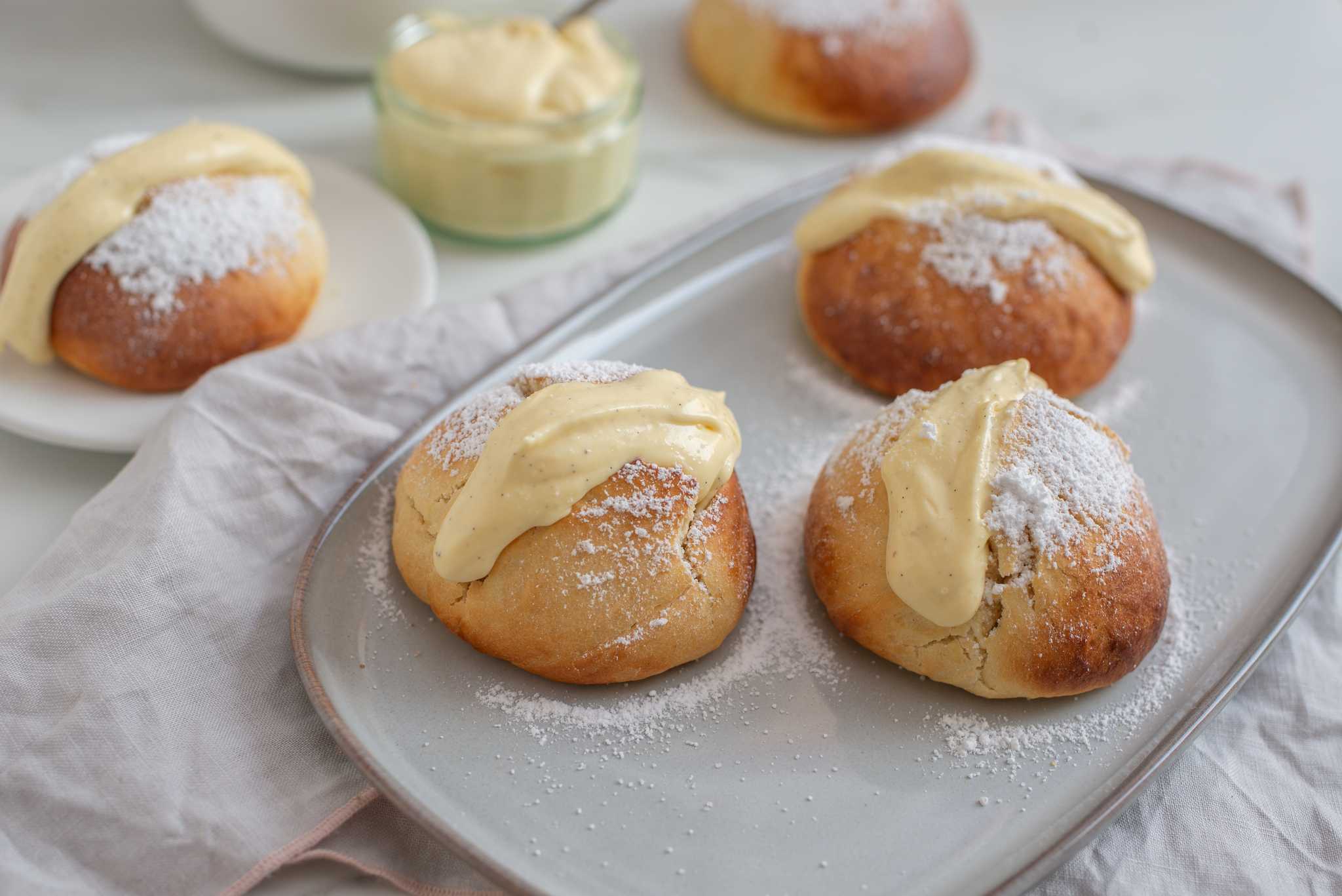 Several maritozzo buns on a white platter on a white table with other buns and filling.