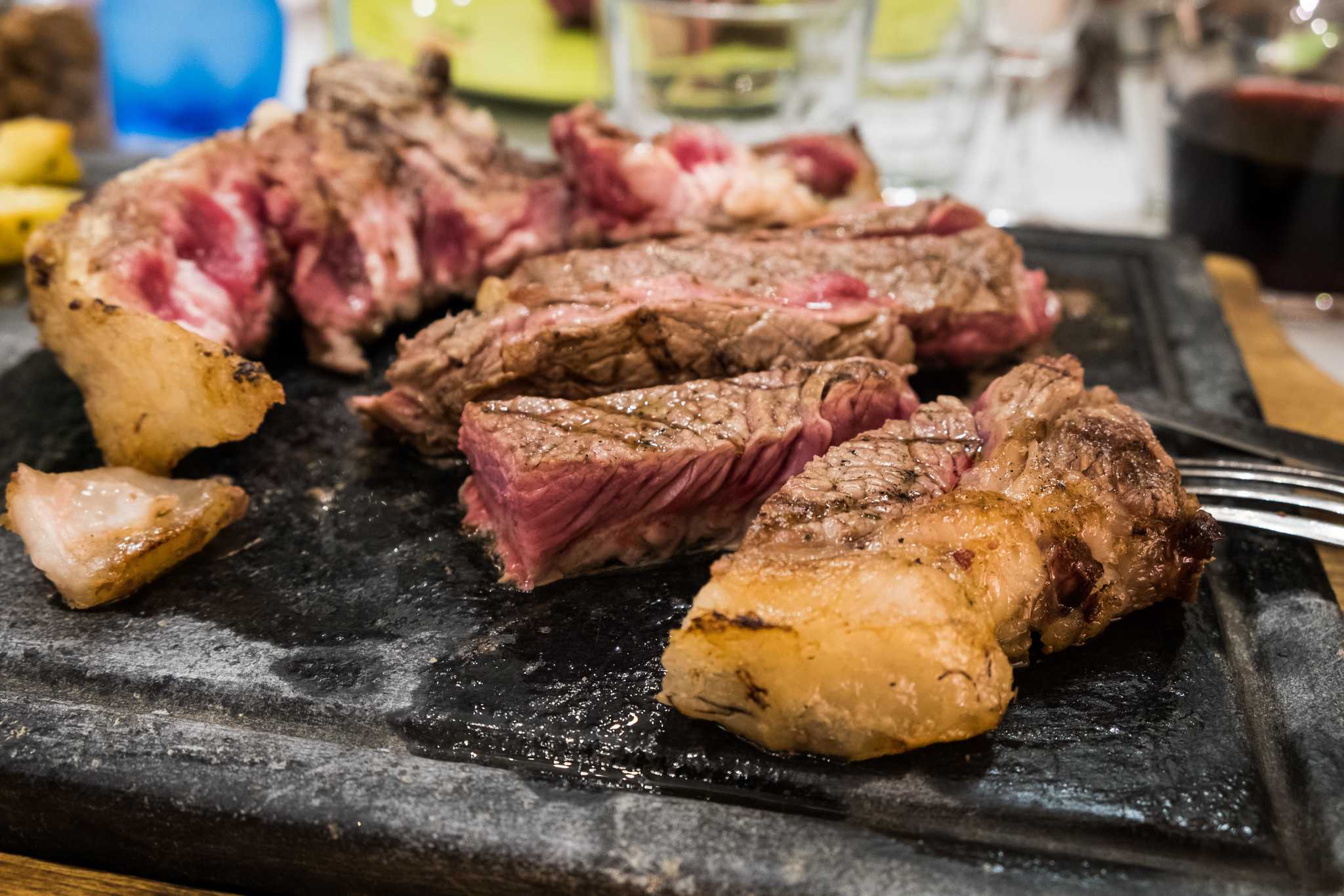 Sliced chunks of rare-cooked steak with roasted potatoes on a black serving board.