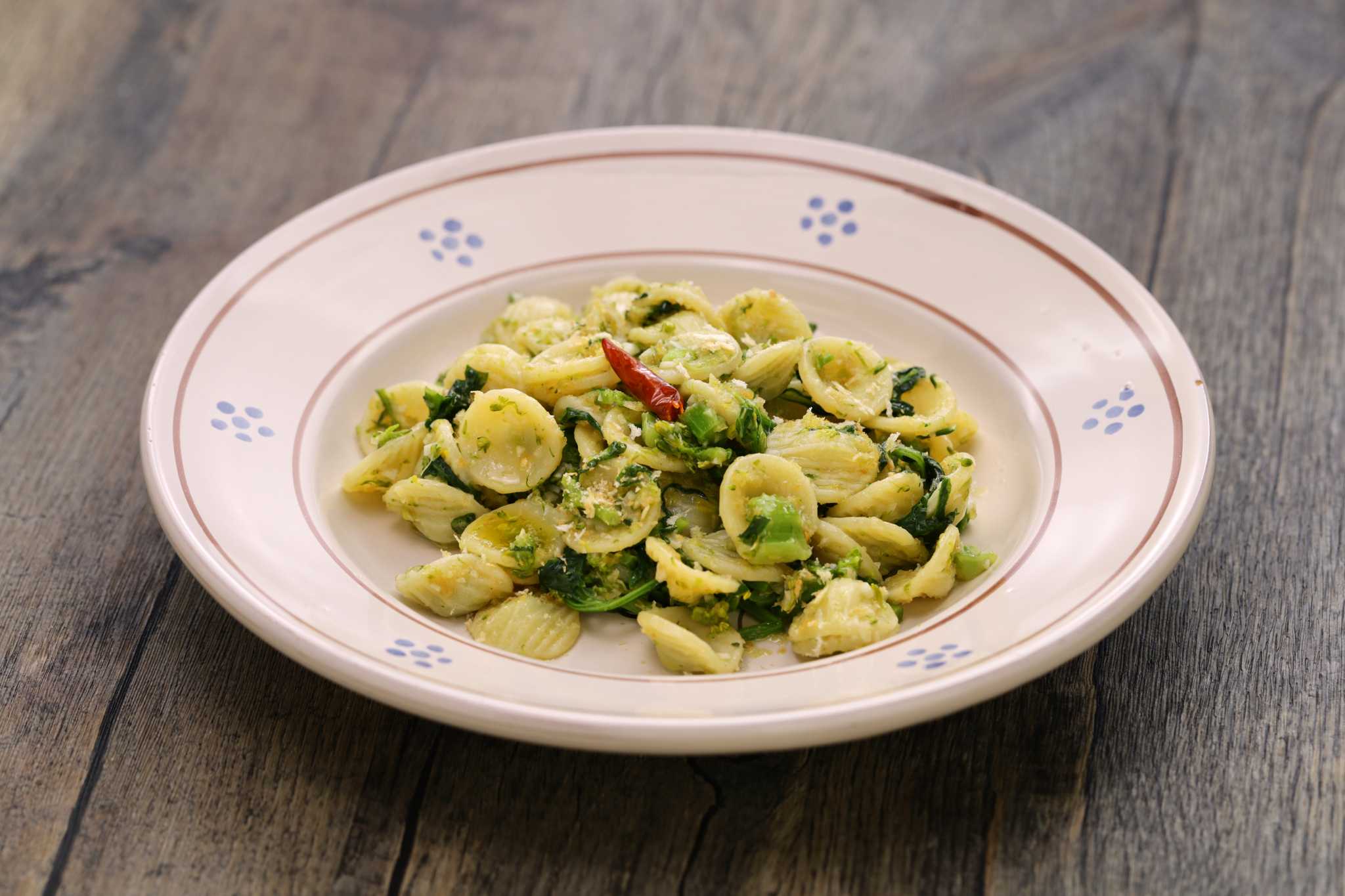 White dish with blue details filled with orecchiette con cime di rapa on a wooden surface.