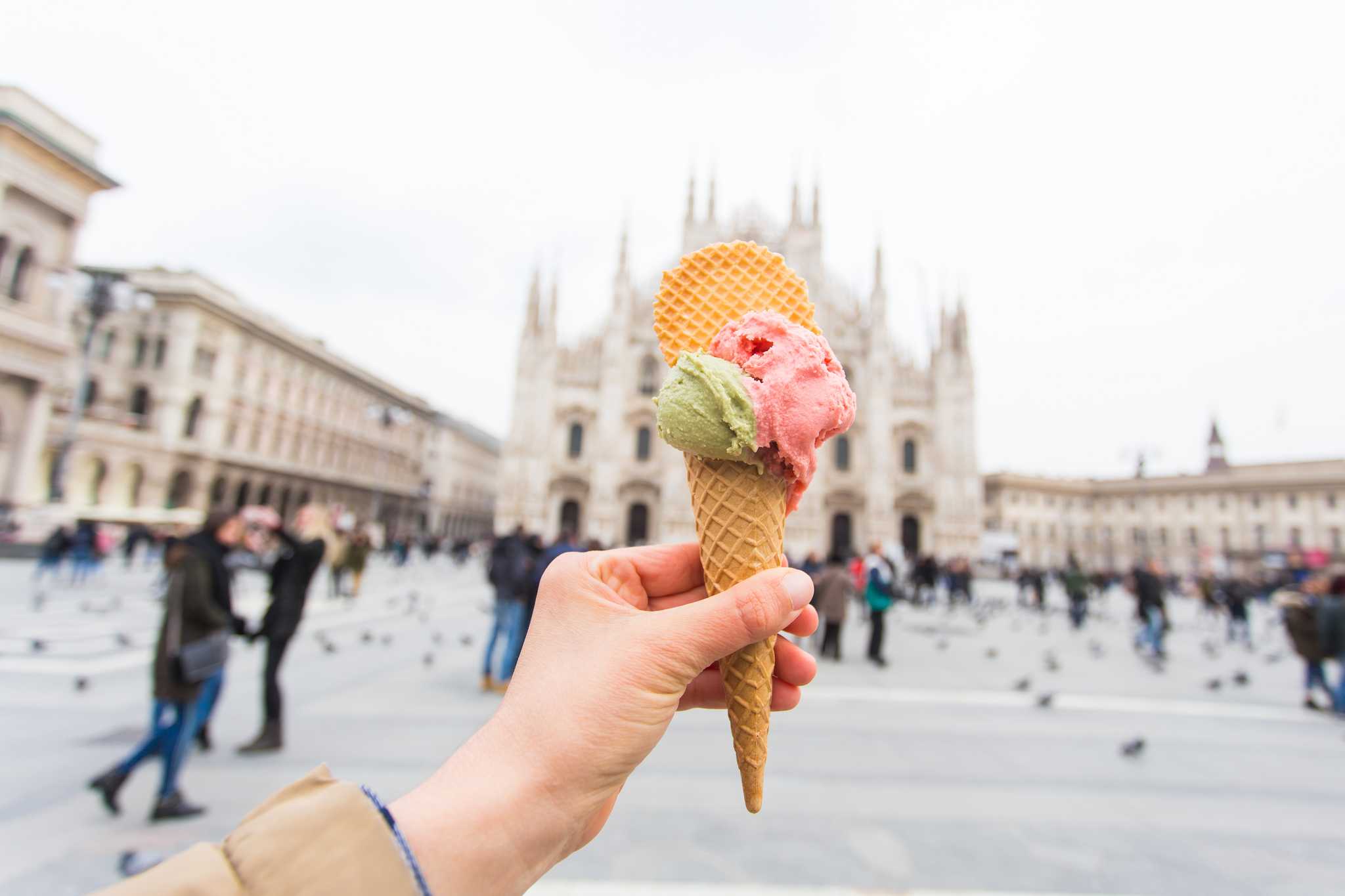 Hand holding cone of green and pink gelato with Milan cathedral in the background.