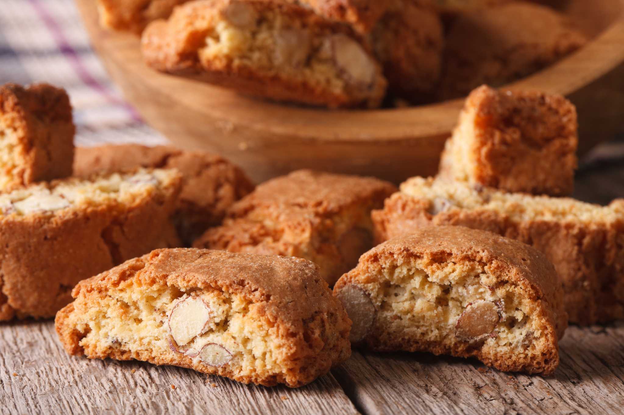 Pile of cantucci beside a wooden bowl filled with more cantucci.