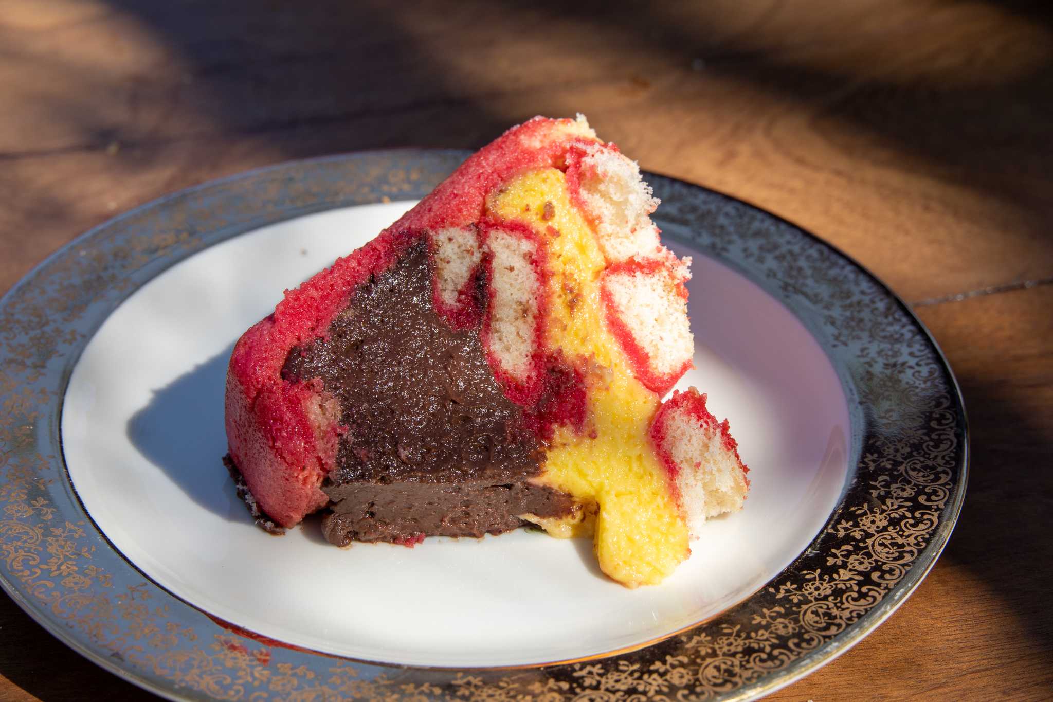 Slice of zuppa inglese on its side on a plate, brown, yellow, and pink layers visible.