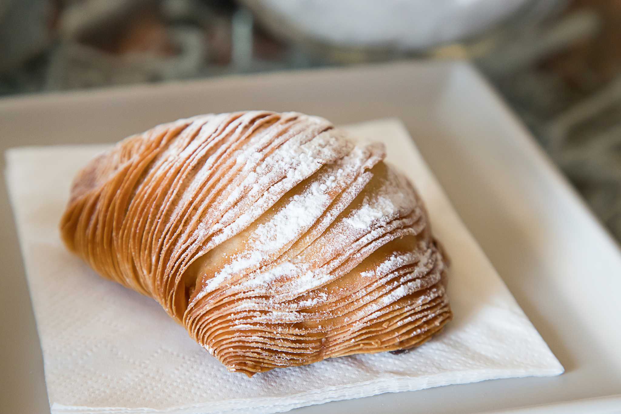 Mant-layered sfogliatella dusted with powdered sugar on a white plate.