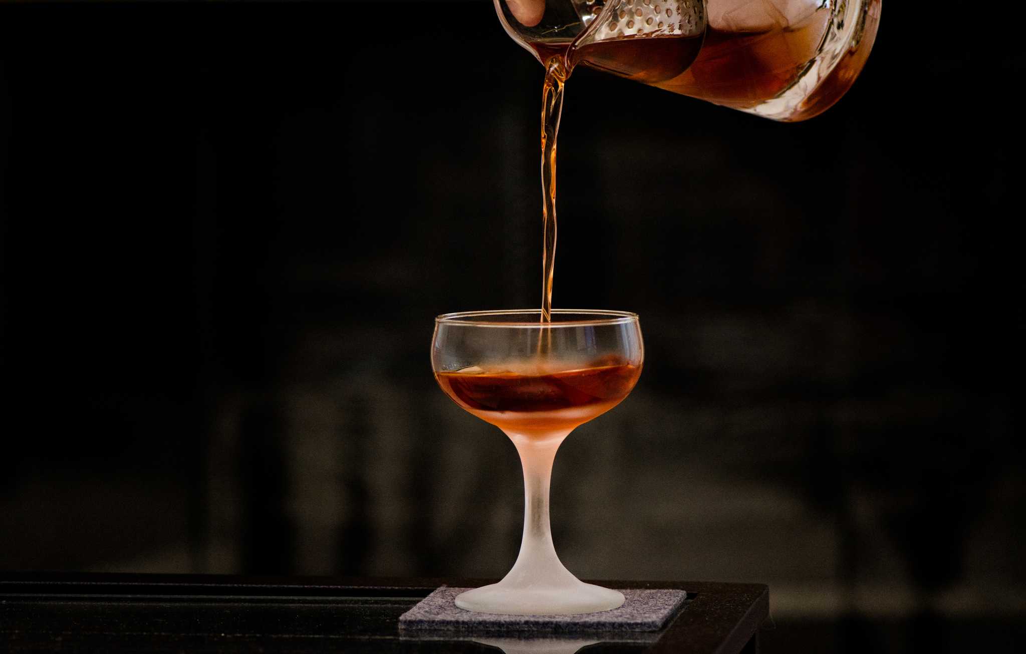 Amaro pouring into a chilled glass from above, set against a dark background.
