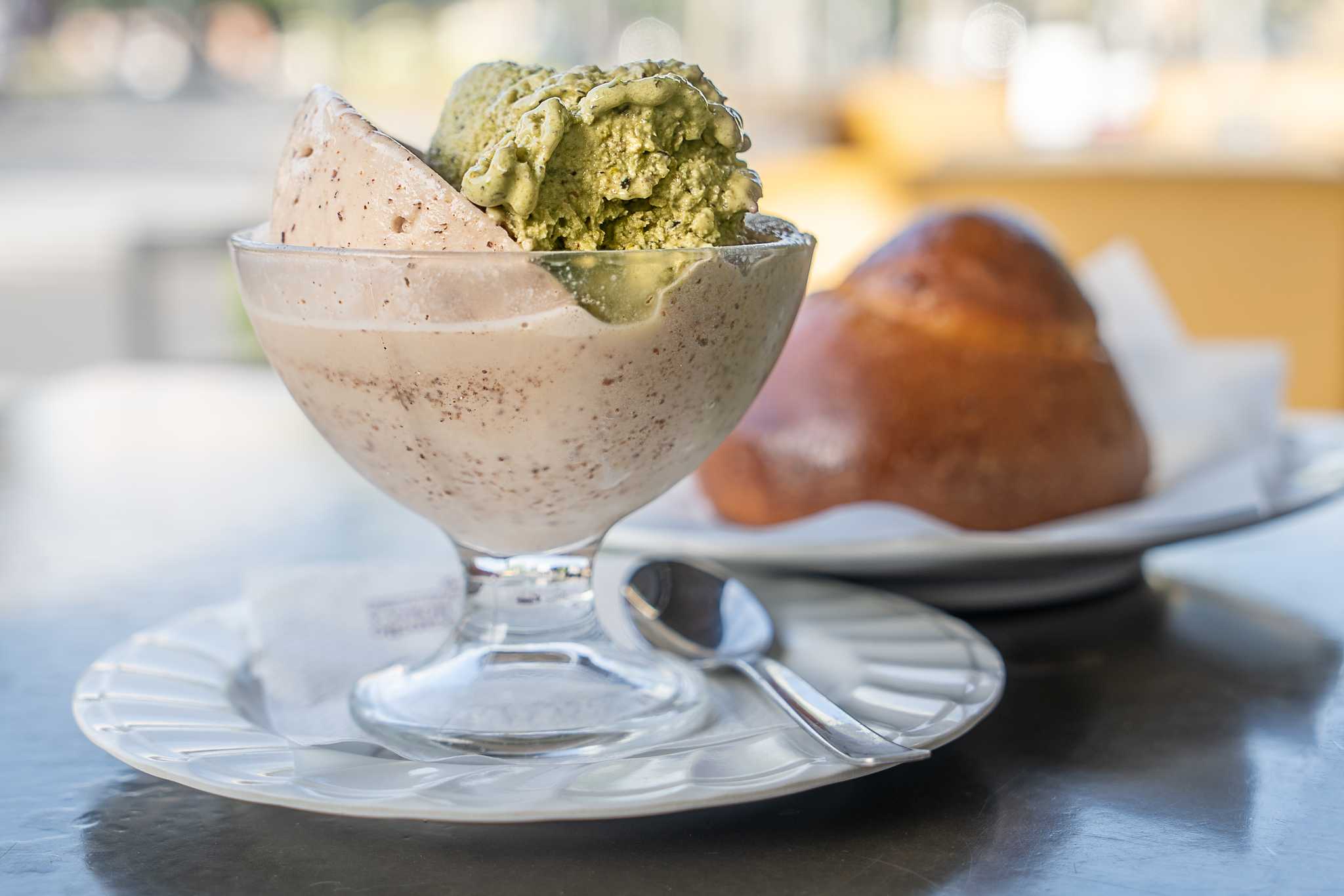 Almond and pistachio granita in a glass dish with a brioche bun in the background.