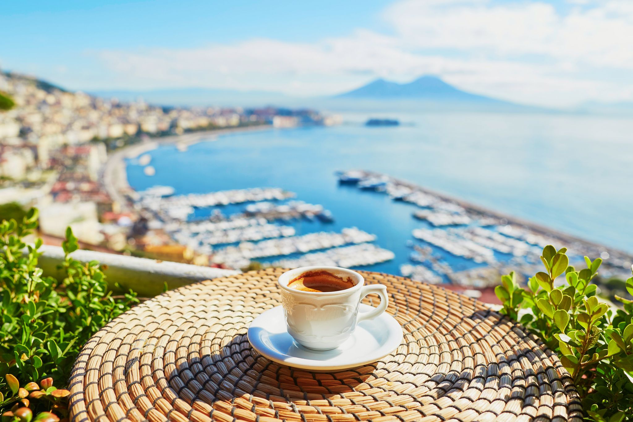 Small white cup of espresso with a view of Mount Vesuvius across the Bay of Naples.