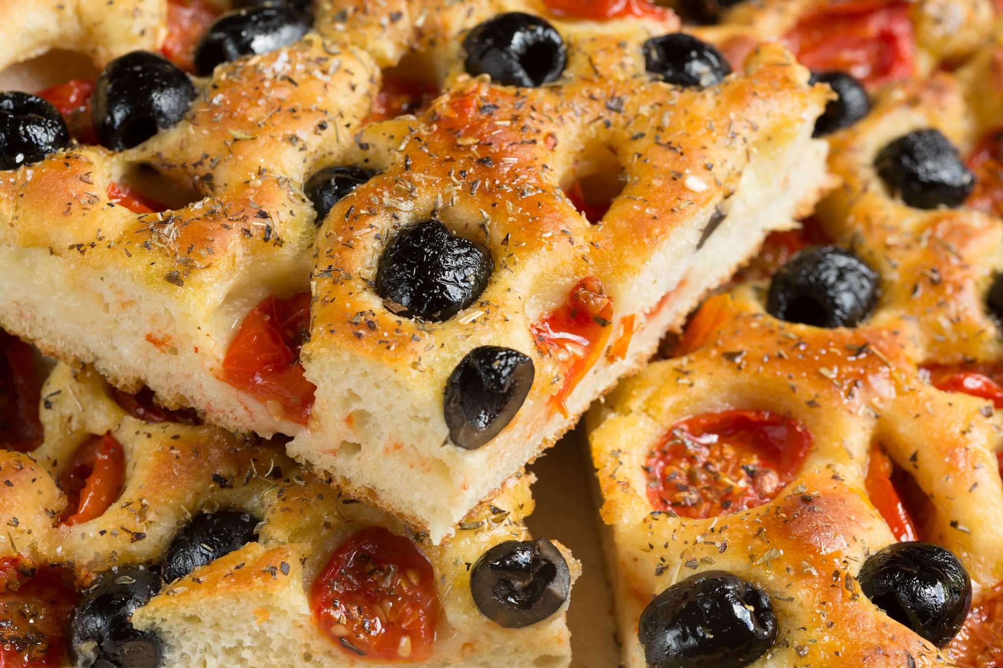 Close-up of sliced focaccia with black olives and cherry tomatoes baked into it.