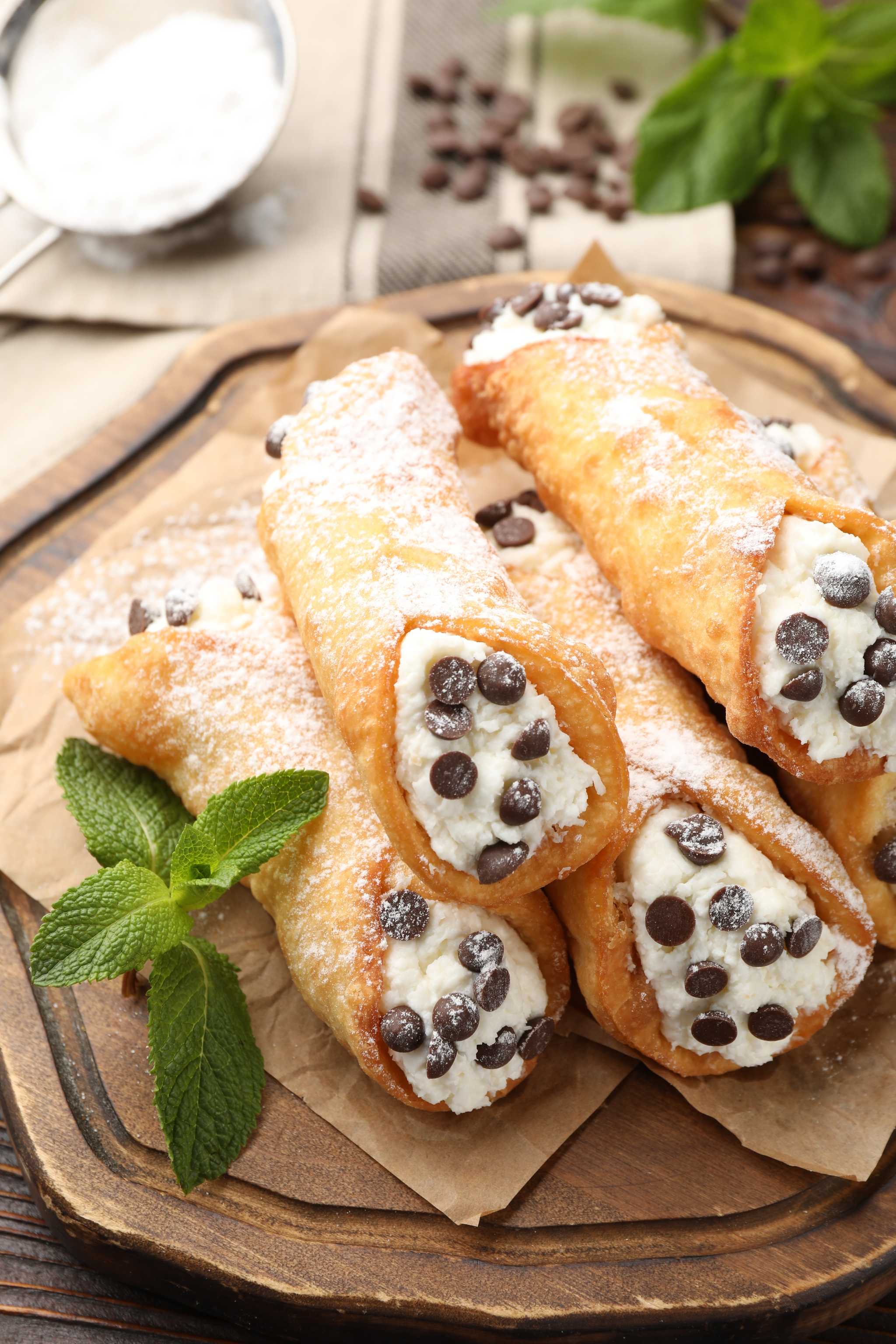 Cannoli with chocolate chips on a tray dusted with powdered sugar and garnished with mint.
