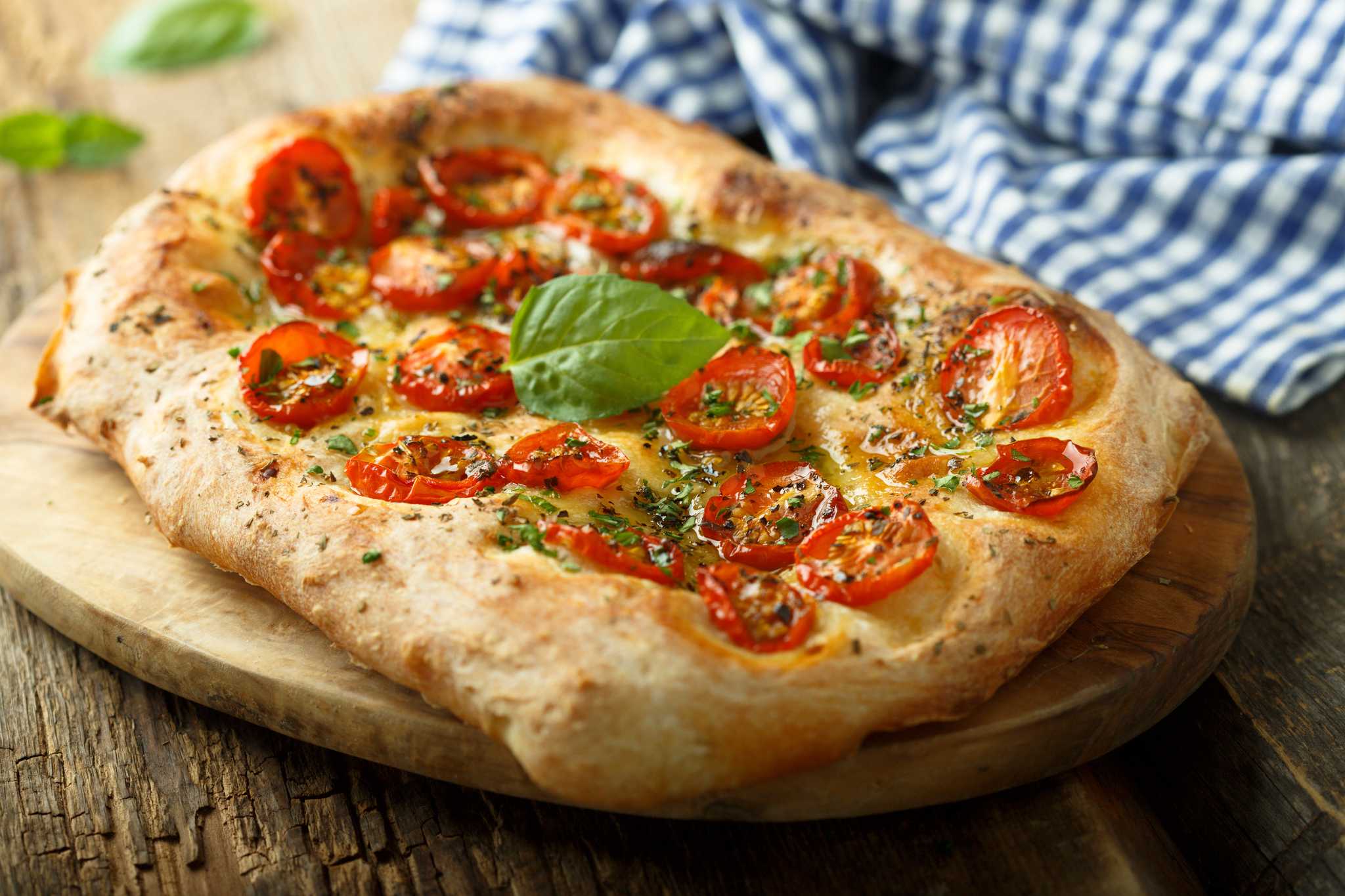 Dimpled flatbread with tomatoes and basil on a wooden cutting board on top of a wooden table.